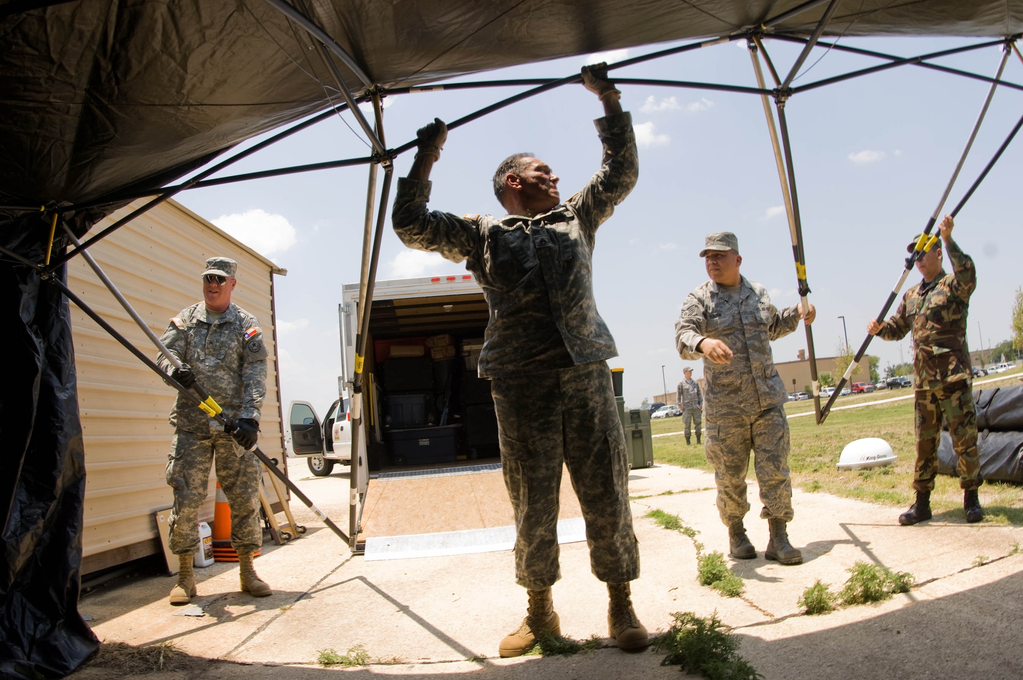 (Left-right) Army Sgt. Marc Jones, Army Staff Sgt. Robert Ribeiro, Staff Sgt. Gonzalo Roman and Master Sgt. Mark Martinez set up a base-X tent, part of the Joint Incident Communications Capability (JICC) that will provide video teleconference, satellite and cellular communications next to the Emergency Operations Center at Brooks City-Base in San Antonio July 22. The Texas Army National Guard is part of the Standing Joint Interagency Task Force-Texas at Camp Mabry, Texas.  Sergeants Jones and Ribeiro are stationed at Bee Caves Armory, Austin, Texas. Sergeants Roman and Martinez are from the Air National Guard's 149th Communications Flight at Lackland Air Force Base, Texas. Once completed the JICC will provide 2000 sq. ft. of portable or tented floor space on the lawns in front of the EOC. (U.S. Air Force photo/Lance Cheung)