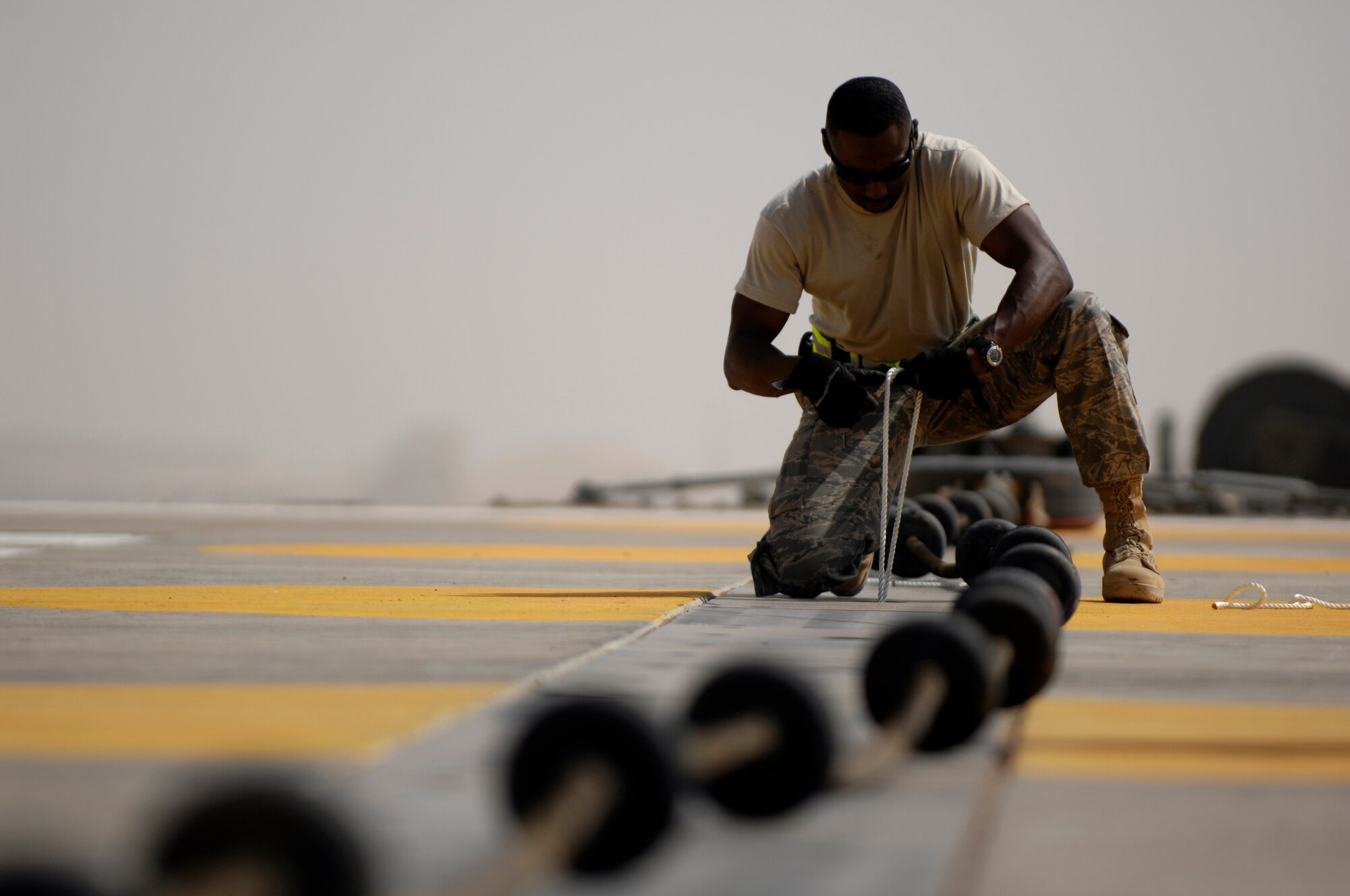 JOINT BASE BALAD, Iraq -- Tech. Sergeant Fred Williams secures rope around the Mobile Aircraft Arresting System cable to the runway here July 20 as part of an annual certification of the system. This system is used to catch aircraft during take off and landing emergencies. Securing its cable to the runway prevents the cable from flying up and damaging the aircraft. Sergeant Williams is the 332nd Expeditionary Civil Engineer Squadron's NCO in charge of barrier maintenance and is deployed from Kadena Air Base, Japan. (U.S. Air Force photo/Airman 1st Class Jason Epley)