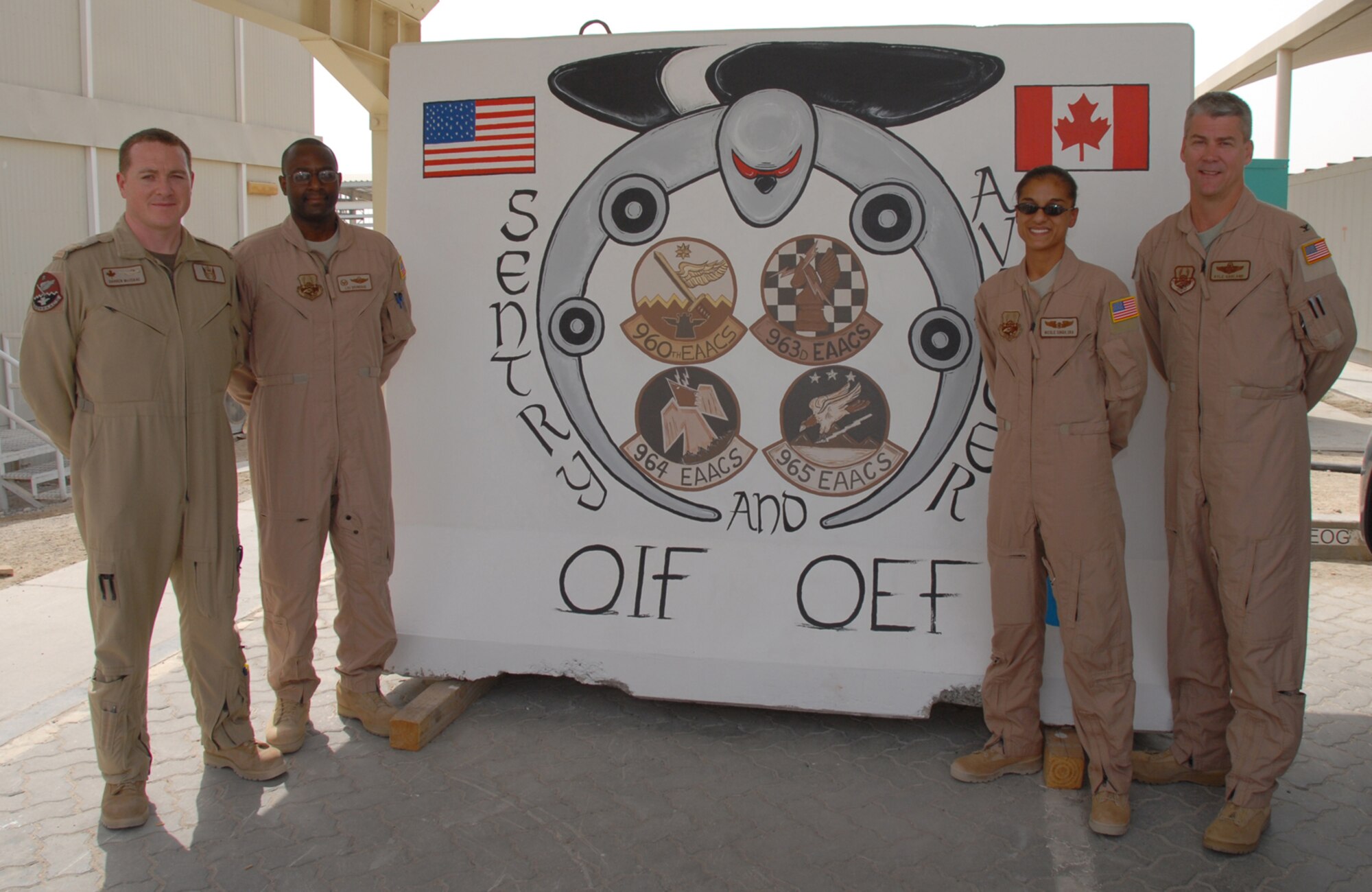 Senior Airman Nicole Singh (right center), an Air Surveillance Technician with the 960th Expeditionary Airborne Air Control Squadron, in front of the mural she painted for the 960th with Col. Kyle Garland (far right), 380th Expeditionary Operations Group Commander, Lt. Col. Lou Brundidge (left center), 960th Expeditionary Airborne Air Control Squadron Commander, and Capt. Darren MacIsaac, Royal Canadian Air Force Senior Director Weapons Controller. (Photo by Tech. Sgt. Christopher A. Campbell)