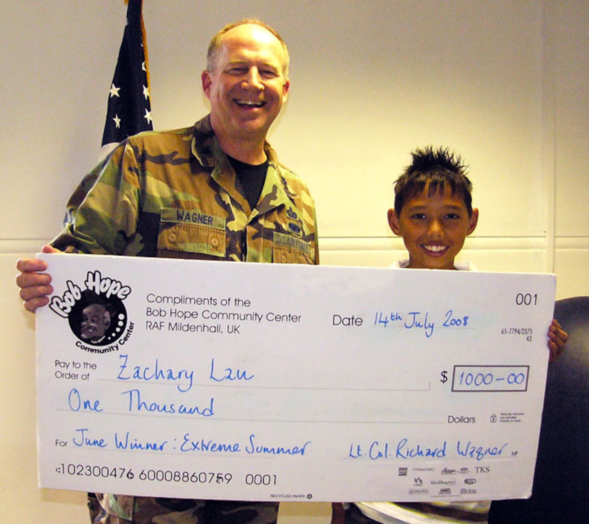RAF MILDENHALL, England -- Lt. Col. Rich Wagner, 100th Force Support Squadron commander, presents a $1,000 check to Zackary Lau July 17. Zackary was the youth category winner of the monthly Extreme Summer prize for June. Each month during the points-for-participation contest there will be four $1,000 cash prizes awarded – one prize per entry category. Everyone with 300 points or more per month goes in for a random drawing. (U.S. Air Force file photo)