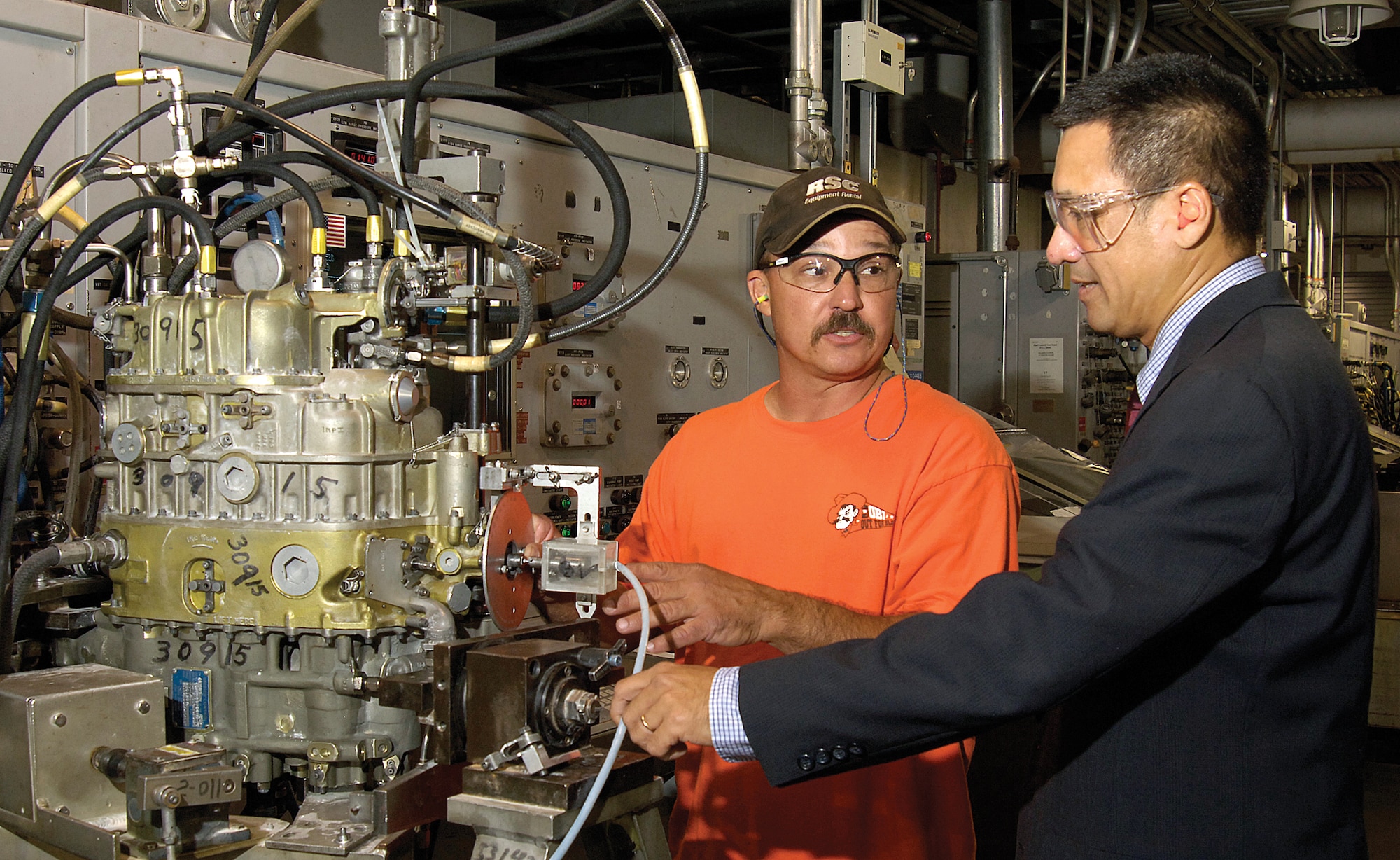 Tinker mechanical engineer Bang Nguyen, right,  and pneudraulics system mechanic John Tschoepe discuss an F100 unified fuel control in the Fuel Accessories Test Facility of Bldg. 3108.  Mr. Nguyen is responsible for keeping the facility and its sensitive equipment functioning, often a challenge with the older test stands that may require repairs of obsolete but critical components.  Mr. Nguyen was a teenager when he was urged to flee Vietnam with two younger siblings as Saigon fell.  Leaving his home, parents and all possessions, he came to America where he would soon teach himself English while attending college.(Air Force photo/Margo Wright)