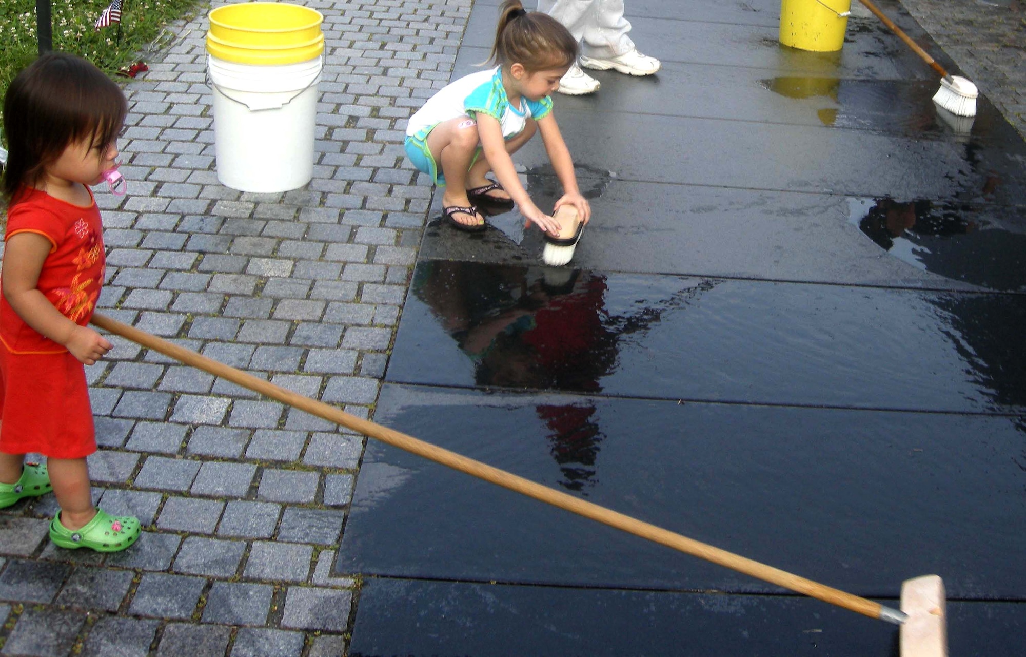 WASHINGTON, D.C. -- Two-year-old Chloe Spangler and 4-year-old Lauren Eckert scrub a pathway that follows the nearly 247-foot Vietnam Memorial Wall here July 20. The volunteer wall washing is a way for service members to thank fallen service members and was conducted under the guidance of the National Park Service. The NPS coordinates volunteers to clean the wall each week, or 52 times per year. At dawn, more than 20 members of the 459th Air Refueling Wing, family and other volunteers stood face to face with their own reflections while washing more than 58,000 names of service members on the wall. Chloe is the daughter of Master Sgt. Camila Eckert (not shown), 459th Mission Support Flight wing career assistance advisor, and Lauren is the daughter of Master Sgt. Sally Spangler (not shown), 459th MSF family support manager. (U.S. Air Force photo/Tech. Sgt. Amaani Lyle)