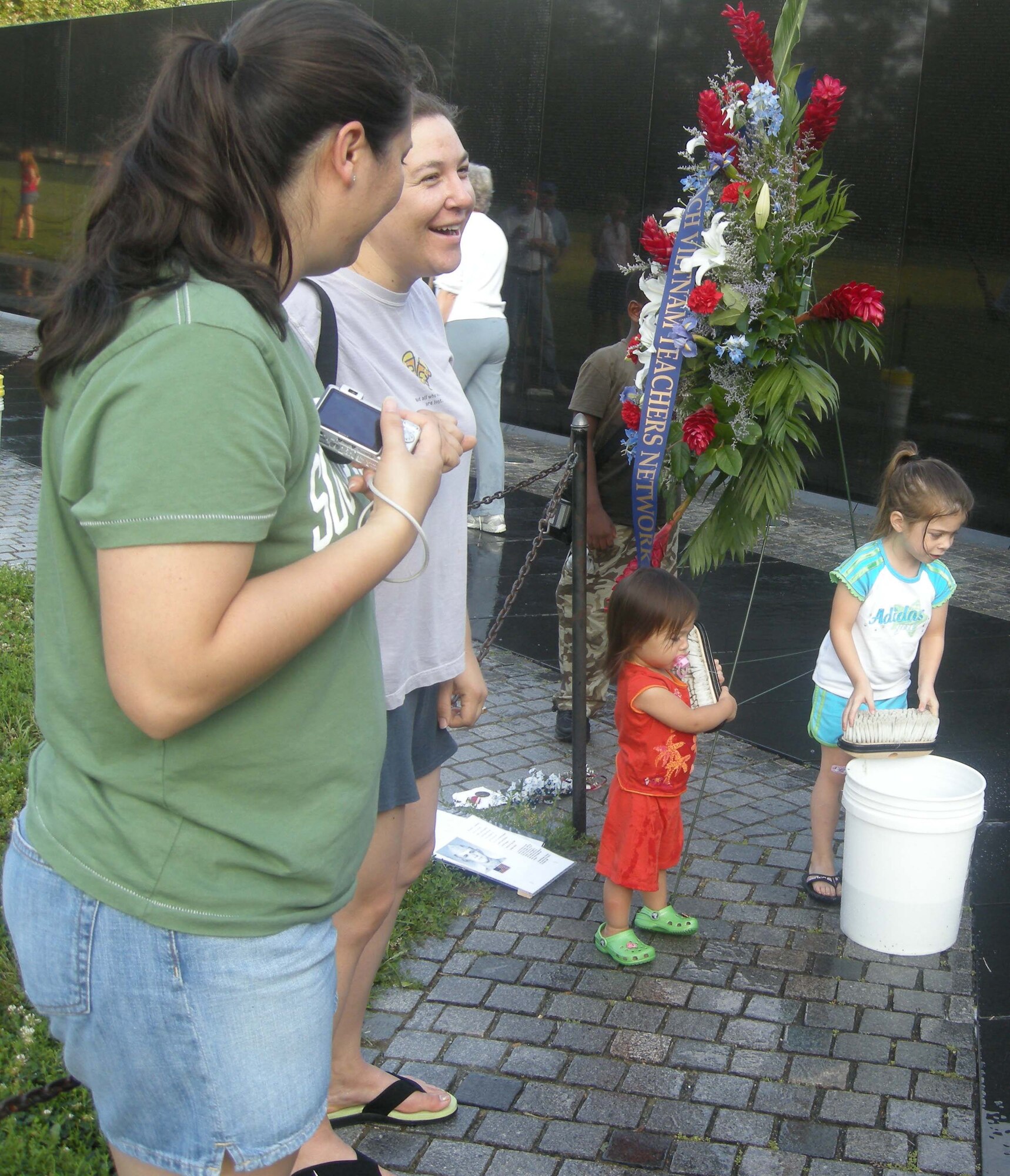 WASHINGTON, D.C. -- Master Sgts. Camila Eckert and Sally Spangler share a laugh as their respective daughters, 2-year-old Chloe and 4-year-old Lauren, prepare brushes to clean the Viet Nam Memorial Wall here July 20. More than 20 members of the 459th Air Refueling Wing, family and other volunteers pose after they stood face to face with their own reflections while washing more than 58,000 names of service members on the nearly 247-foot Viet-nam Memorial Wall. Sergeant Eckert is the wing career assistance advisor with the 459th Mission Support Flight and Sergeant Spangler is the family support manager with the 459th MSF. (U.S. Air Force photo/Tech. Sgt. Amaani Lyle)