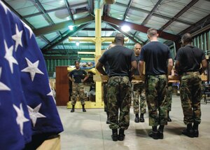 Honor Guard trainees in a warehouse on base use a wooden frame to simulate a casket.  The Airmen use the frame in order to learn pallbearer movements used during funeral ceremonies the Honor Guard performs.