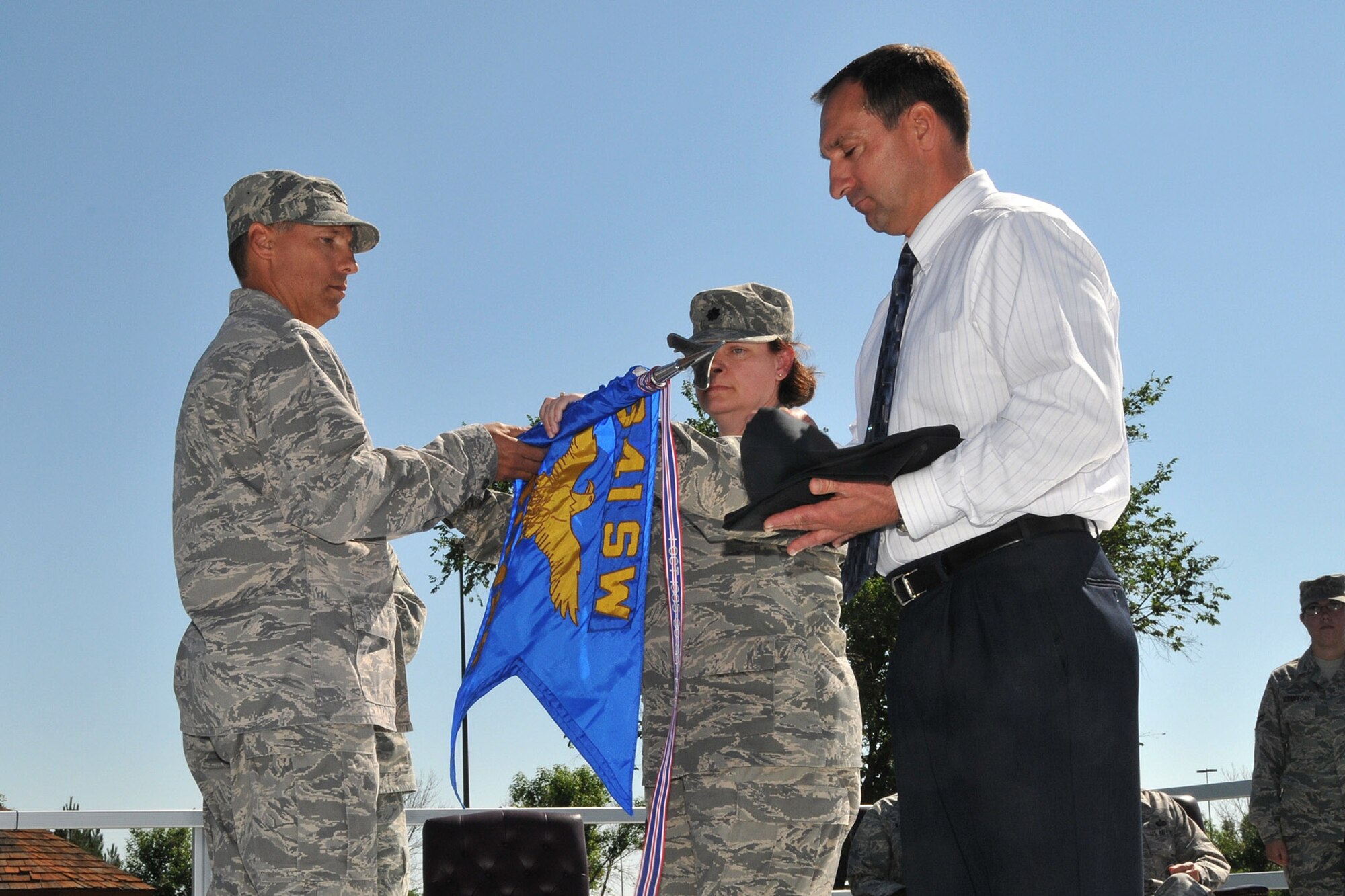 Lt. Col. Karyn Wright, 341st Mission Support Squadron commander assists Col. Roderick Davis, 341st Mission Support Group commander with rolling up the 341st MSS guidon for retirement. Manpower and Personnel Flight Chief Brian Jolly stands ready to place it in its protective cover. The event took place during the merger ceremony of the 341st MSS with the 341st Services Squadron July 17. (U.S. Air Force photo/John Turner)