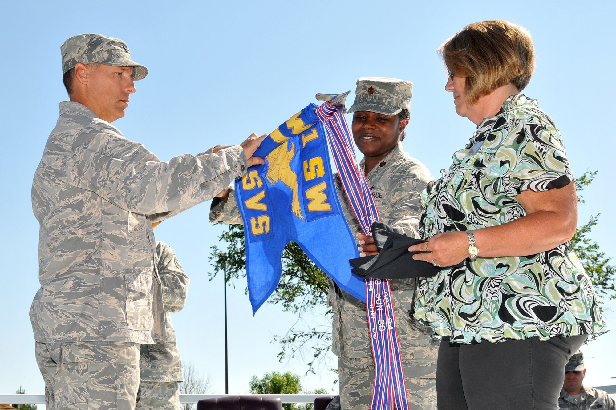 Maj. Rosalyn Walker, 341st Services Squadron commander assists Col. Roderick Davis, 341st Mission Support Group commander, with rolling up the 341st SVS guidon for retirement. Nonappropriated Funds Human Resources Officer Cindy Hill stands ready to place it in its protective cover. The event took place during the merger ceremony of the 341st SVS with the 341st Mission Support Squadron July 17. (U.S. Air Force photo/John Turner)