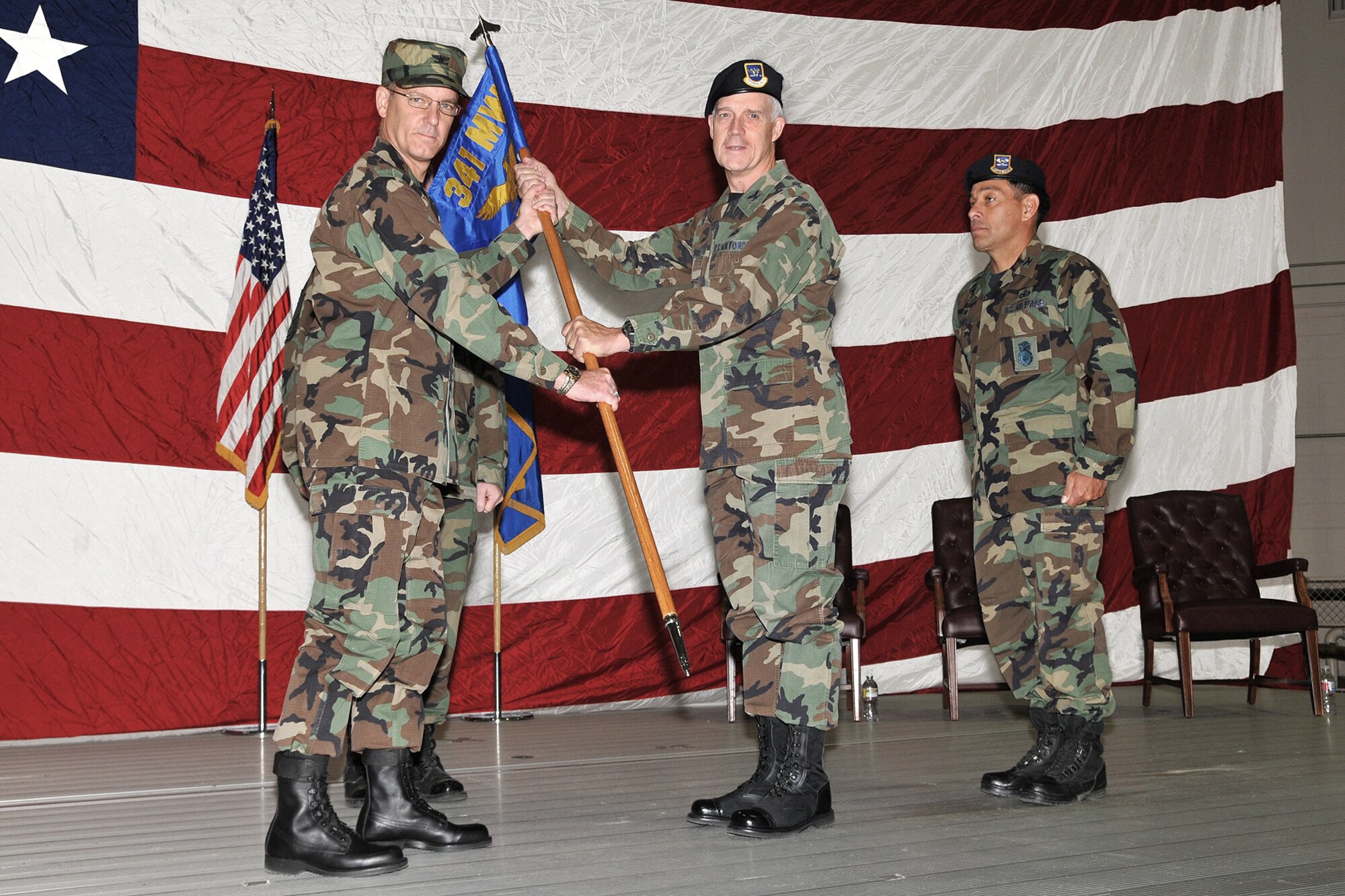 Col. Michael Fortney, 341st Missile Wing commander, passes the 341st Security Forces Group guidon to Col. John Probst in a change of command ceremony in the 3-BayHangar July 18. Outgoing 341st SFG commander Col. Steve Asher looks on. (U.S. Air Force photo/John Turner)