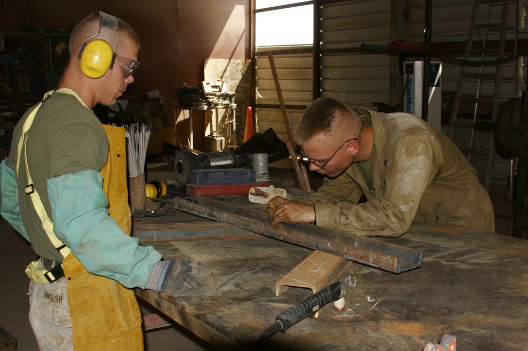 Sergeant Jason Walsh and Cpl. John James, metal workers with Marine Wing Support Squadron 172, Marine Wing Support Group 37, 3rd Marine Aircraft Wing (Forward), construct a smaller version of their bracket. The bracket afforded security forces a way to mount security equipment on top of towers around the air base.