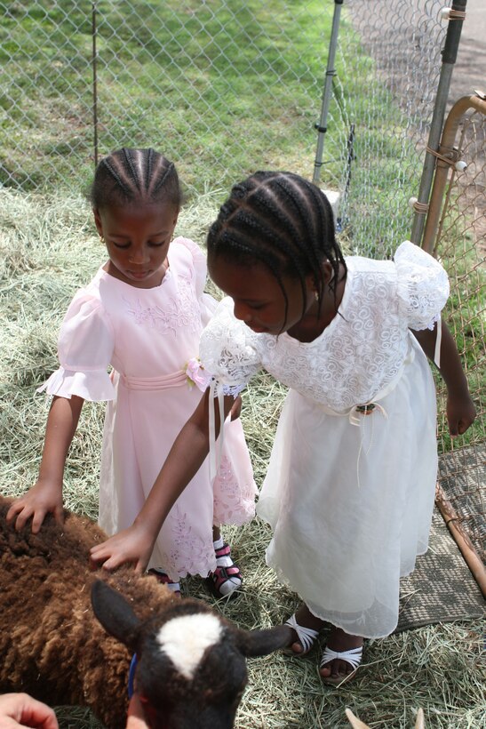 Maria (left) and Elizabeth, daughters of Petty Officer 2nd Class Ademola Junaid, religious programer for U.S. Marine Corps Forces, Pacific, pet goats at a mobile petting zoo during the Headquarters and Service Battalion family day July 25 here.