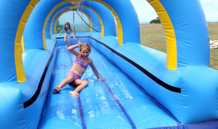 Ariel, step daughter of Sgt. Wendell Smith, the maintenance noncommissioned officer in charge for U.S. Marine Corps Forces, Pacific Motor Transportation, slides down the slip-and-slide as her sister Jewels prepares to follow her, during the HQ&SVC BN family day July 25 here.