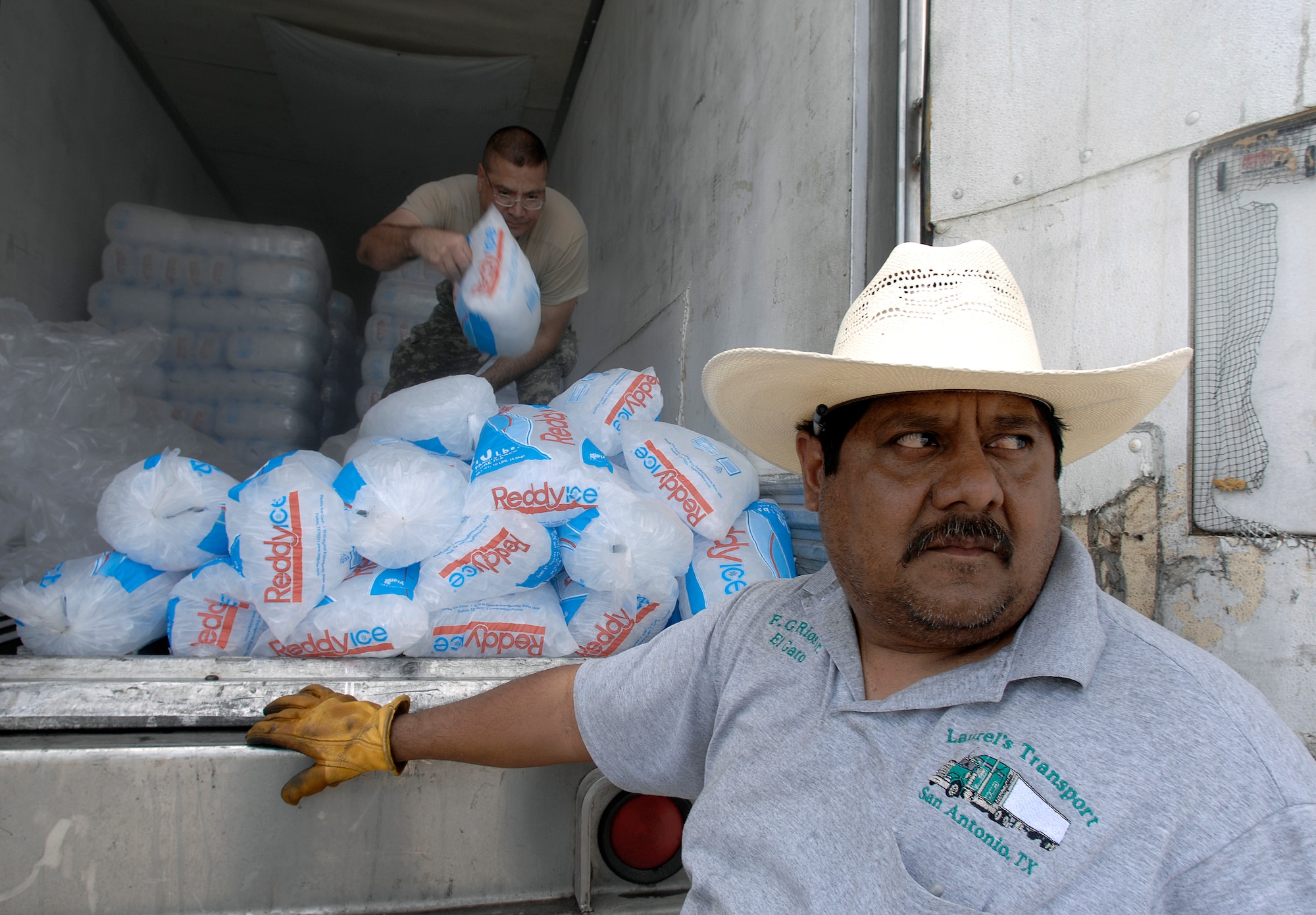Truck driver Fernando Rios watches hurricane victims arriving from South Padre Island, Texas, looking for relief aid July 24 while U.S. Army Specialist Luis Dominguez prepares bags of ice to be loaded into vehicles. Texas Task Force 1 members passed out nearly 4,000 bags of ice, 50 tons of water and 1,200 self-heating meals to vicitims of Hurricane Dolly. Specialist Dominguez is stationed with the 133rd Aviation Battalion at New Braunfels, Texas. (U.S. Air Force photo/Staff Sgt. Bennie J. Davis III)