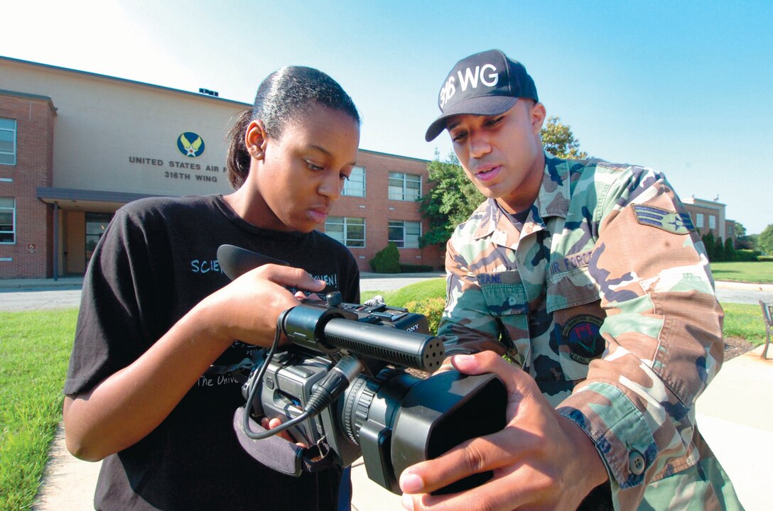 Senior Airman Chris Crane, 316th WIng Public Affairs videographer, trains Janiqua Robinson, 16, on a digital video recorder for man-on-the-street interviews. Janiqua is the daughter of Army Sergeant 1st Class (ret.) Paul M. Robinson. Janiqua finished a video class in school last year. The video training experience that she acuires as a volunteer will help her when she starts a class in television production as a junior next year.