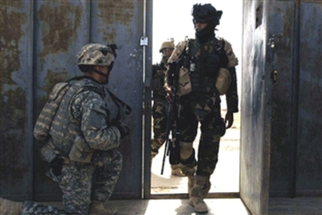 Iraqi soldiers enter the gate of a suspected improvised rocket assisted mortar factory while U.S. Army Spc. Jose Guerra III, left, pulls security, in Shula, Iraq, July 19, 2008. Guerra is assigned to the 101st Airborne Division's 1st Battalion, 502nd Infantry Regiment.  