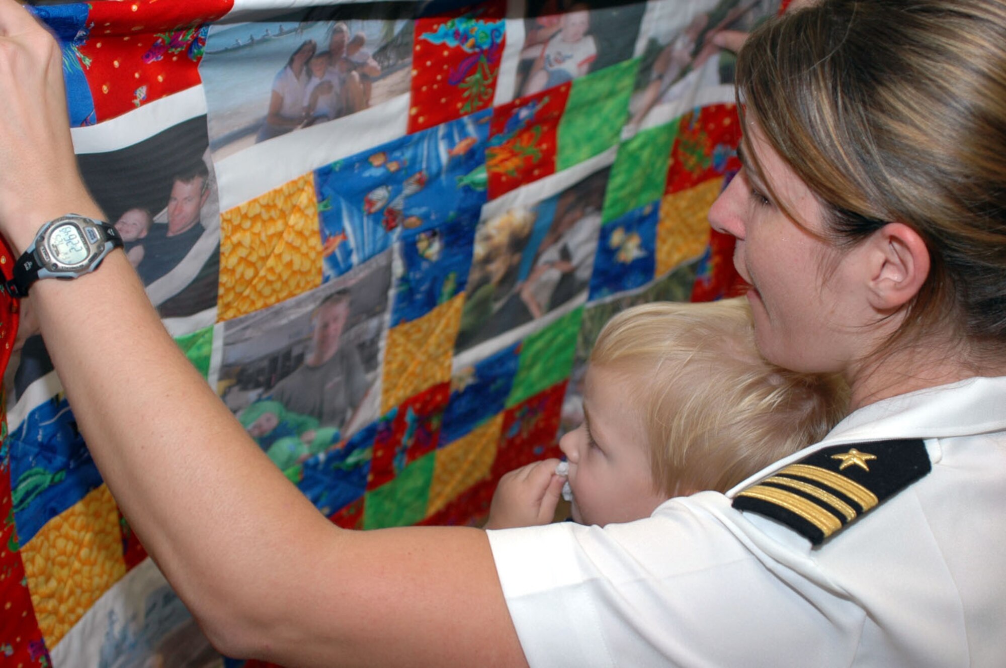 Lt. Cmdr. Jeannie Groeneveld, a speechwriter for U.S. Pacific Fleet, holds up a quilt to show her son.  The quilt is made from family photos and given to her free-of-charge via the Armed Services YMCA's "Operation Kid Comfort" program. Groeneveld's husband Lt. Cmdr. John Groeneveld is a naval aviator deployed on the USS Gridley (DDG 101). Operation Kid Comfort provides quilts to children of deployed service members. (U.S. Navy photo/Mass Communication Specialist 3rd Class Byung Cho)