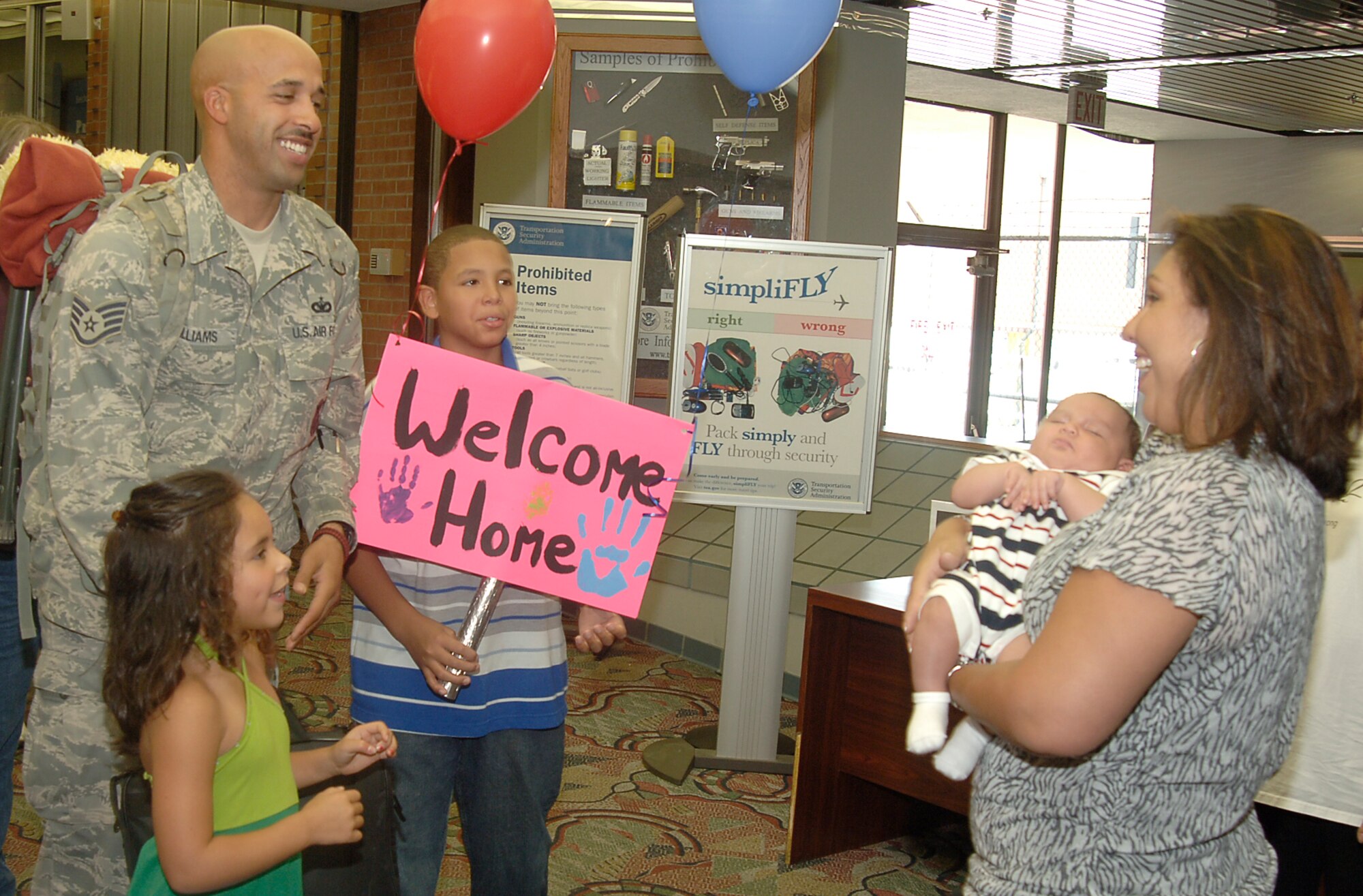 MCCONNELL AIR FORCE BASE, Kan.  --  Staff Sgt. Terrance Williams’s family greets him at Wichita Mid-Continent Airport, July 27,  as he returns home from a six-month deployment to Balad Air Base, Iraq. His wife, Tech. Sgt. Nichol Williams, son, Dante, 11, daughter, Jazzy, 6, and six-week-old baby, Terrance waited with a sign and balloons to welcome him home. Sergeant Williams was one of 13 22nd Security Forces Squadron Airmen who were reunited with their loved ones. (Photo by Airman 1st Class Jessica Lockoski)