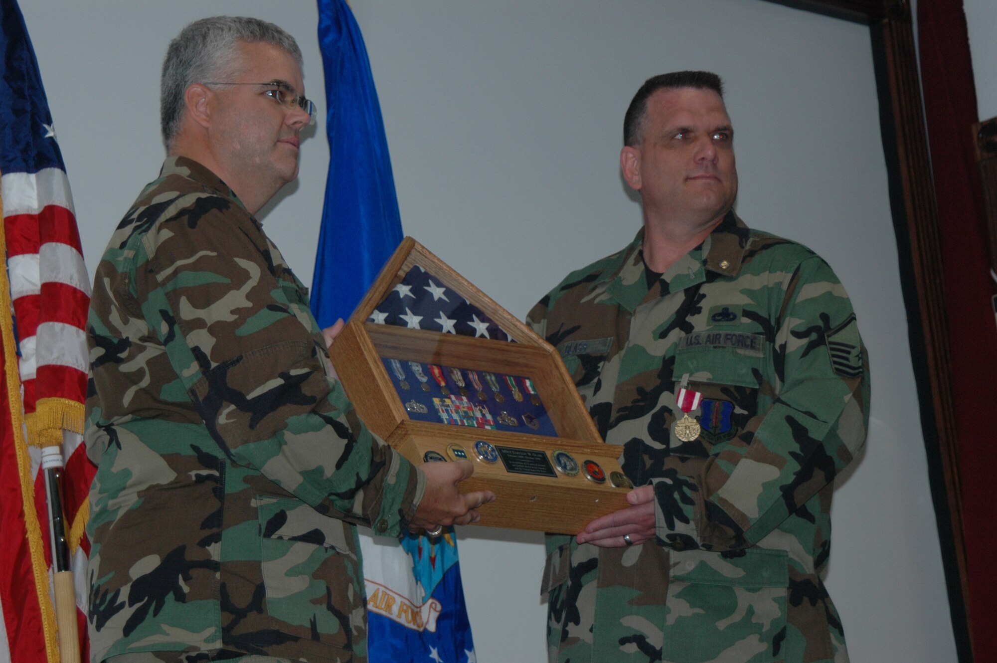 Master Sgt. Glass receives a shadow box from Maj. Michael Shetler, 325th Maintenance Operations Squadron commander during his retirement ceremony July 29.  The box highlights awards and medals Sergeant Glass received since his Air Force career began 23 years ago when he and his twin brother attended basic and technical training together. Both brothers retired this summer.