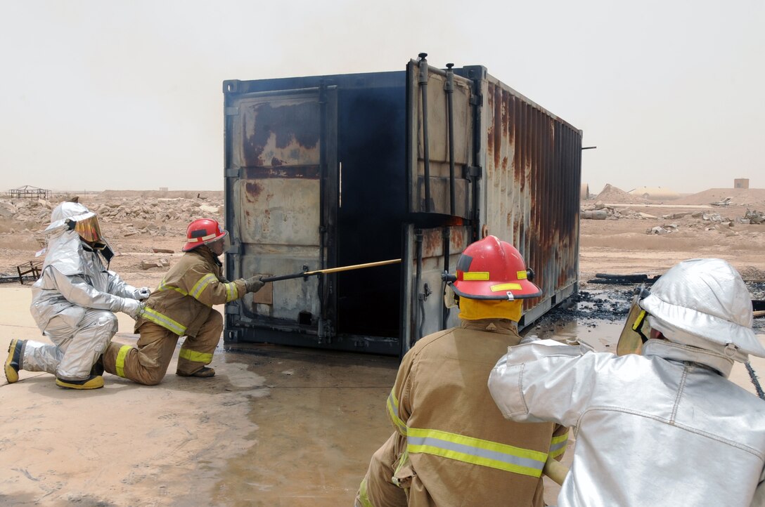 ALI BASE, Iraq -- Staff Sgt. Scott Herbert and Senior Airman Aaron Brackett, 407th Expeditionary Civil Engineer Squadron firefighters, instructs local Iraqi firefighters on the proper usage of the pike pole and advanced hand-line techniques while putting out a fire in a burning training container during a live fire exercise here June 2. The Air Force firefighters provide continuous training to local Iraqi firefighters, which equips them with basic firefighter skills to better serve their communities. Sergeant Herbert is deployed from Ellsworth AFB, S.D and Airman Brackett is deployed from Elmendorf AFB, Alaska. (U.S. Air Force photo/Tech. Sgt. Sabrina Johnson)