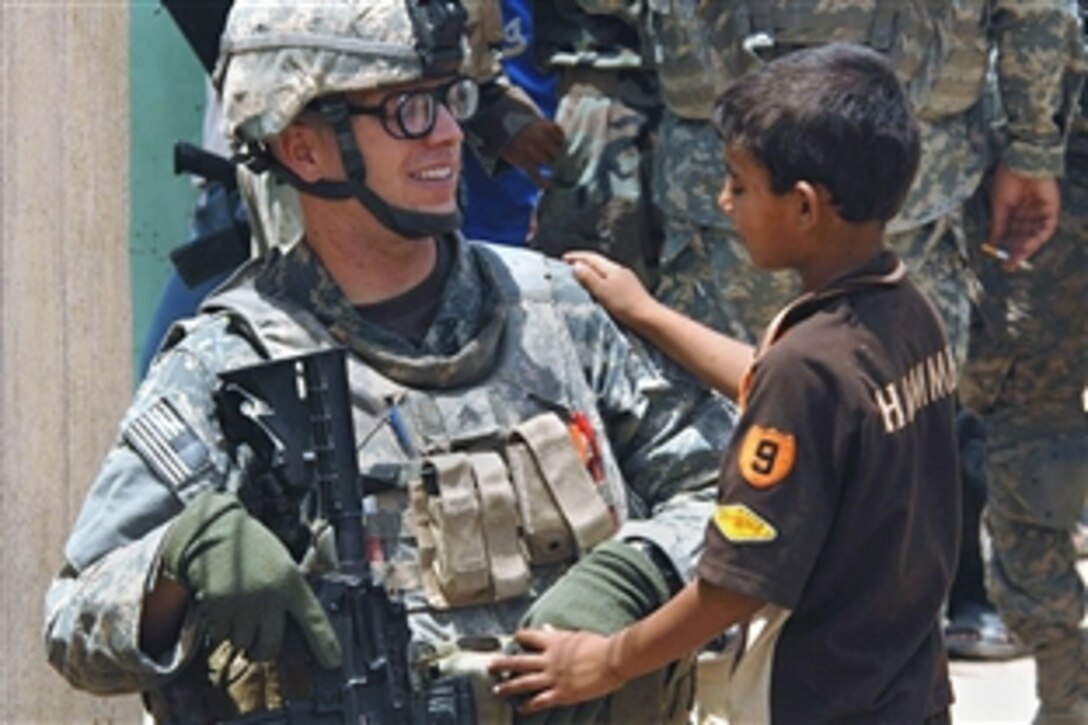 U.S. Army Sgt. Vincent Ruiz talks with an Iraqi child outside a school where Iraqi men are signing up for a local neighborhood watch program in the Sadr City district of Baghdad, May 30, 2008. Ruiz is assigned to the 404th Civil Affairs Battalion.  