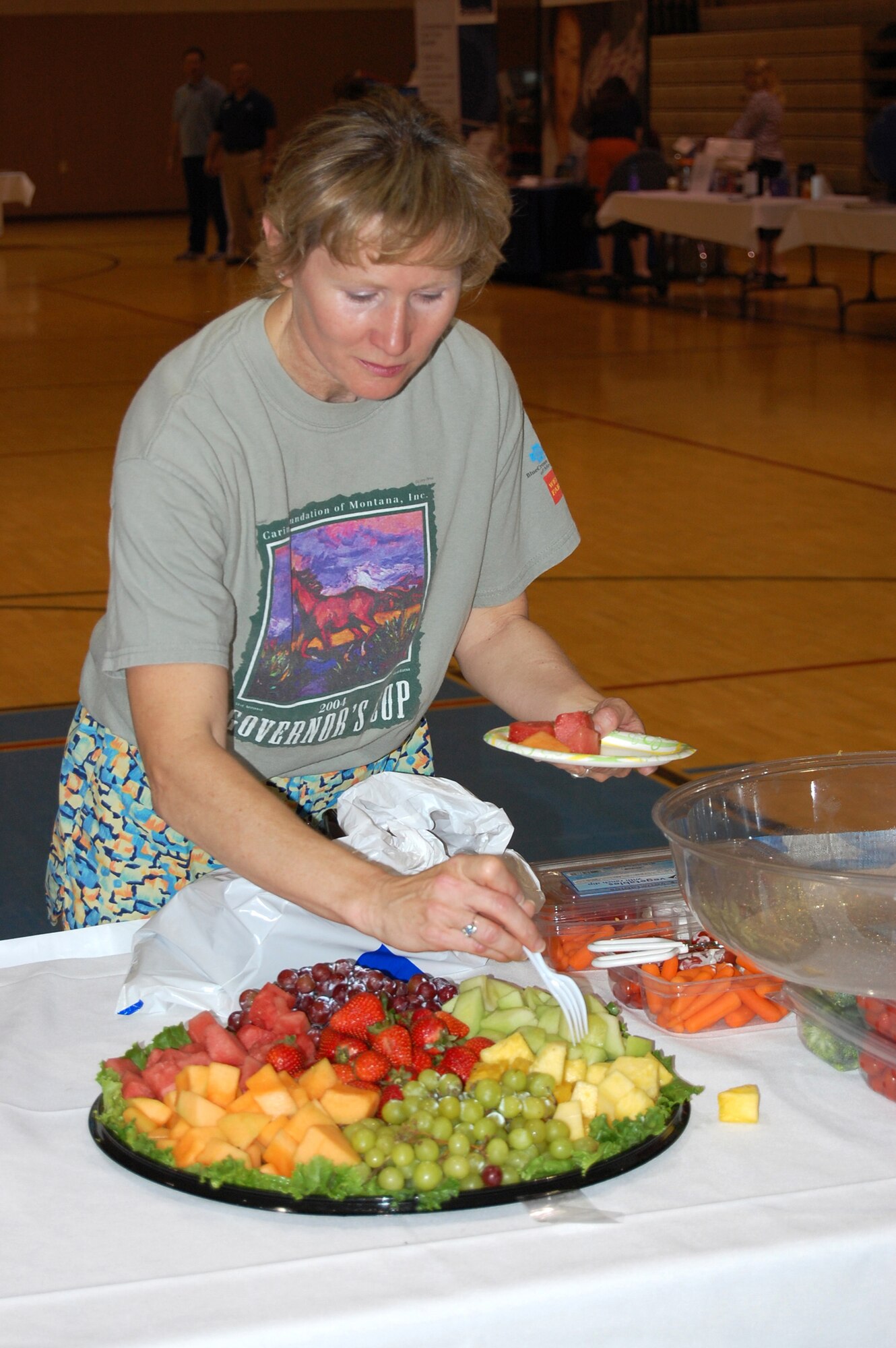 Trish Indreland, 819th RED HORSE Squadron secretary, selects fruit to add to her plate at the health fair hosted by the 341st Services Squadron in the lower gym of the base fitness center May 30. Those in attendance were offered a variety of fitness items from jump ropes to water bottles. Medical professionals from Benefis Health Care were also performing blood pressure checks and handing out information on men's and women's cardiovascular health. (U.S. Air Force photo/Airman 1st Class Dillon White)