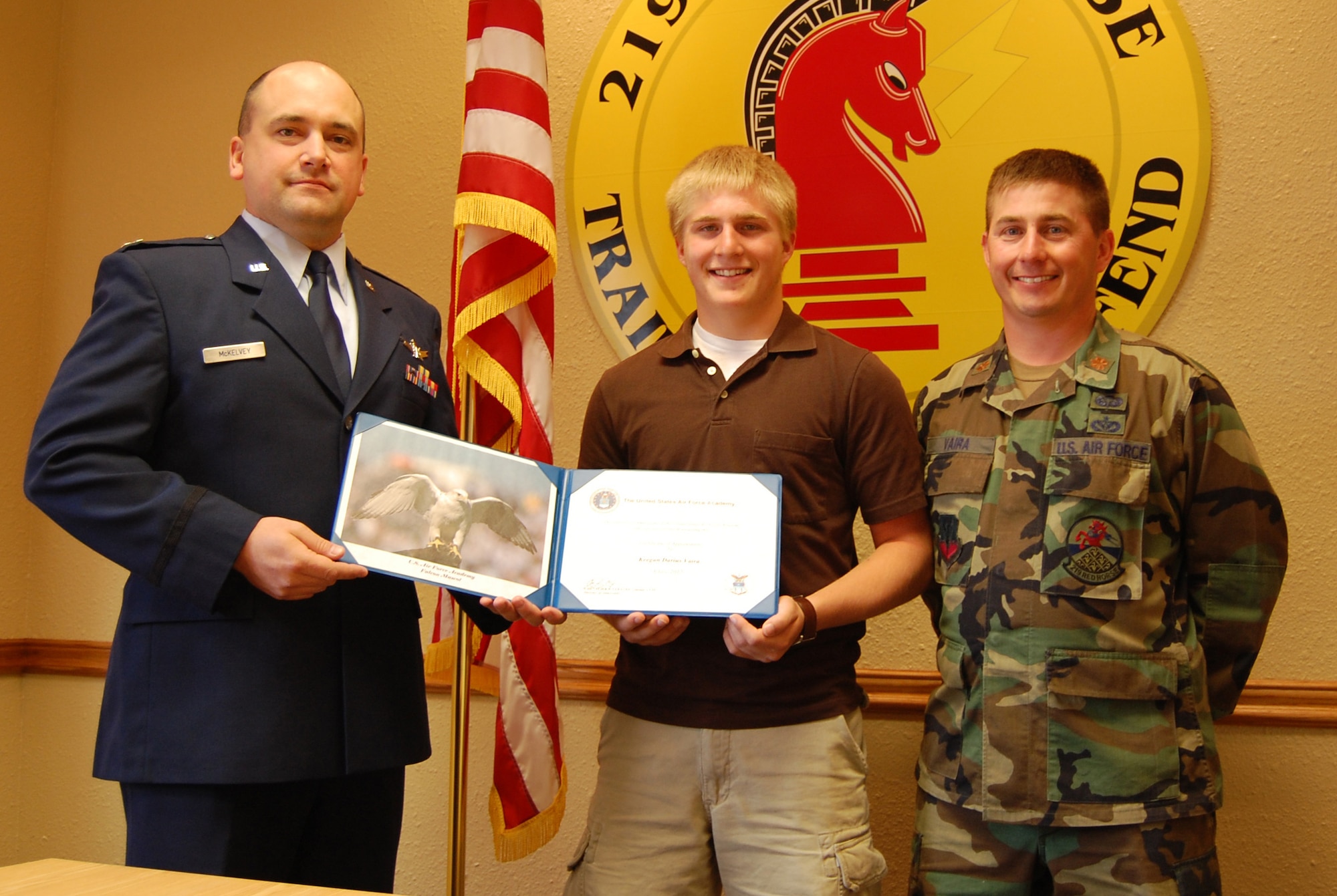 Maj. Conn McKelvey, United States Air Force Academy liaison officer, presents a USAFA certificate of acceptance to  Keegan Vaira, with his father, Maj. Rusty Vaira, 219th RED HORSE Squadron operations flight commander, as a witness at the 219th RED HORSE Squadron Tuesday. (U.S. Air Force photo/Airman 1st Class Dillon White) 