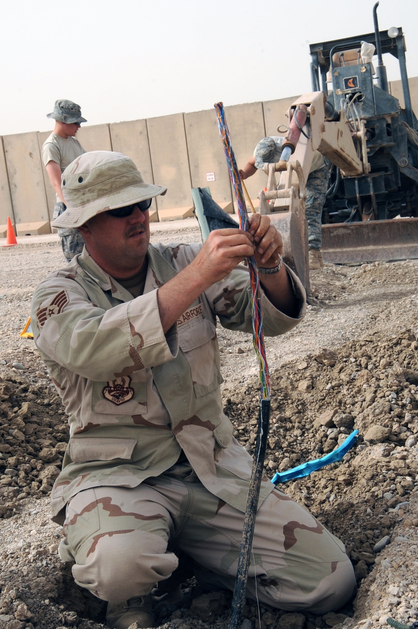 ALI BASE, Iraq -- Staff Sgt. Ray Stetler, noncommissioned officer in charge of base information and infrastructure, prepares the 50 pair copper cable for splicing as Staff Sgt. Javiel Ladines (back right) and Staff Sgt. Timothy Johnson (back left) hand digs for the other side of the cable here June 3. The cables are used to connect telephone and internet lines as a part of the new tents to trailers project. Sergeant Stetler, Ladines, and Johnson are deployed to the 407th Expeditionary Communications Squadron from the 3rd Combat Communications Group at Tinker AFB, Okla. (U.S. Air Force photo/Tech. Sgt. Sabrina Johnson) 