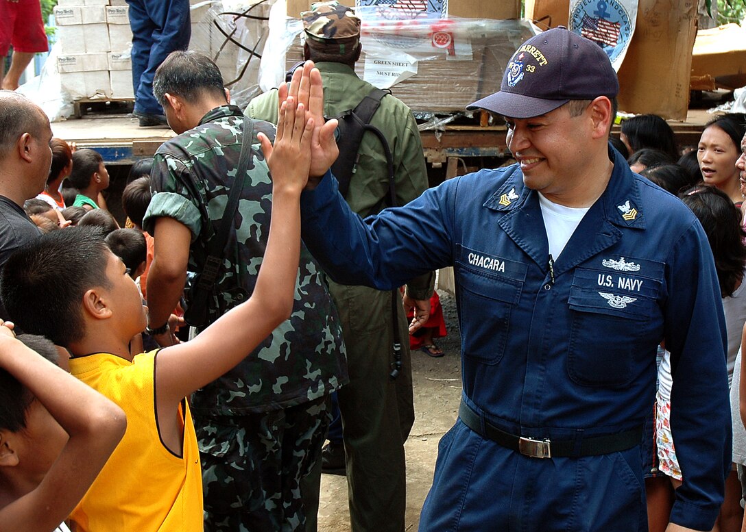 U.S. Navy sailor Carlos Chacara, a personnel specialist, smacks a high-five with a student at West Central Elementary School, June 2, 2008. Crews from U.S. Navy and Coast Guard ships, and Philippine navy seamen, unloaded pallets of donated basic home supplies to be distributed to the needy living near the school. 