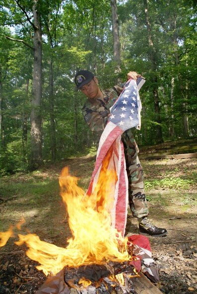Tech. Sgt. John Bankston carefully lowers a flag in the fire, bringing closure to what may been years of service. (Photo by Philip Lorenz III)