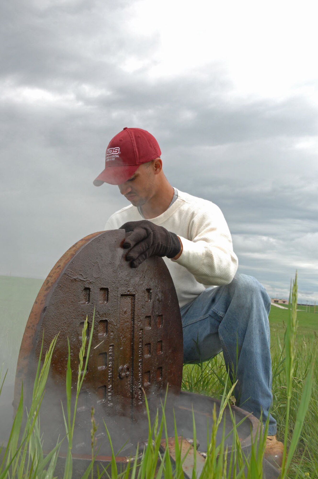 Jason Harris, American Digital Services sewer line smoke tester, lifts a manhole cover to observe smoke during sewer smoke testing Ellsworth Air Force Base, S.D., June 6, 2008. The smoke flow helps identify cracks and other defects; these defects will be worked on later by field crews. (U.S. Air Force photo/Airman Corey Hook)

