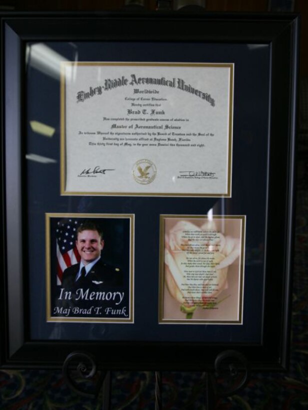 A framed master's degree in aeronautical science accompanies a photo of Maj. Brad Funk and a poem during an Embry-Riddle Aeronautical University graduation ceremony June 6 at Sheppard Air Force Base, Texas. Major Funk, killed during a training Mission May 1, was posthumously awarded his degree by the university. (U.S. Air Force photo/Lt. Col. Ternell Washington)