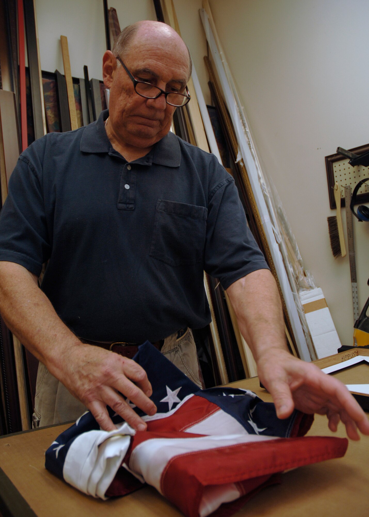 Fred Downs folds an American flag for a retirement shadow box at 10:55 a.m., 1455 ZULU, at the Arts and Crafts Center at Charleston AFB June 4. Mr. Downs is the Arts and Crafts Center's picture framer and painter. (U.S. Air Force Photo/Airman 1st Class Timothy Taylor)
