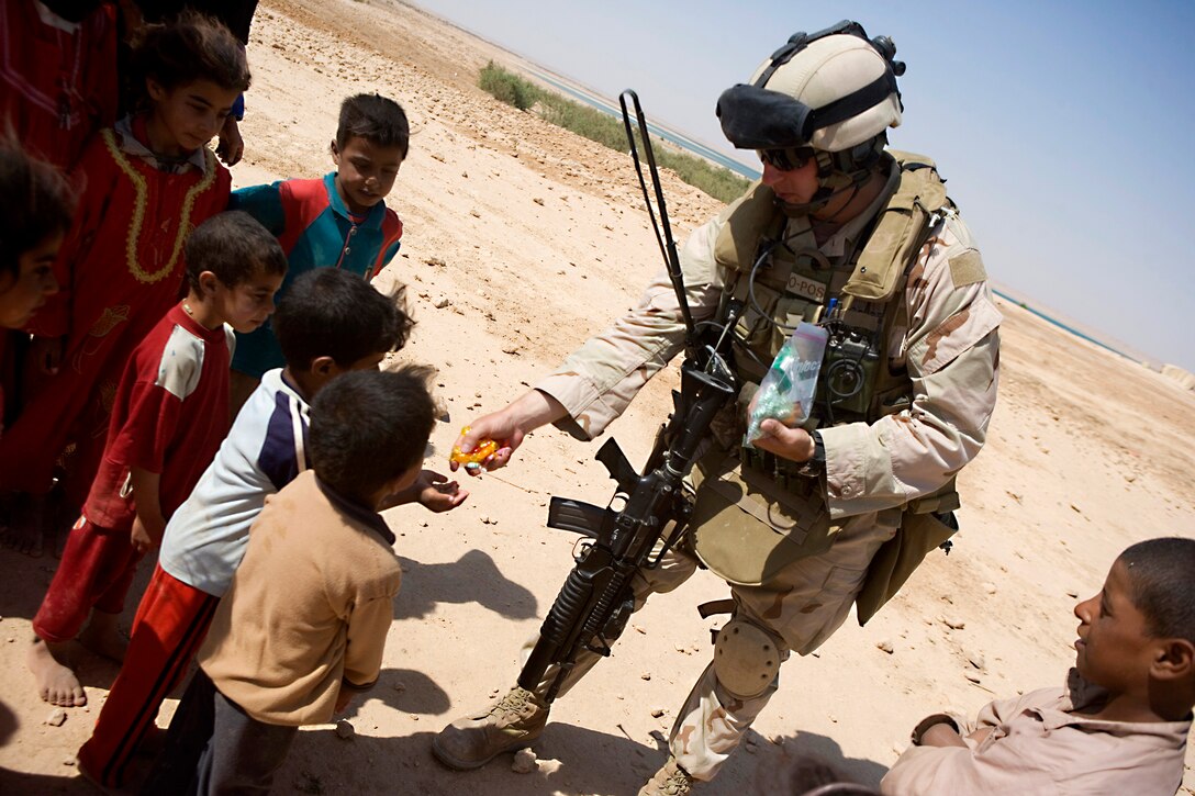 U.S. Navy Petty Officer 1st Class Clayton Alek-Finkelman hands out candy to children while on patrol north of Haditha Dam in Anbar, Iraq, June 5, 2008. He is assigned to Regimental Combat Team 5's Riverine Squadron 3.