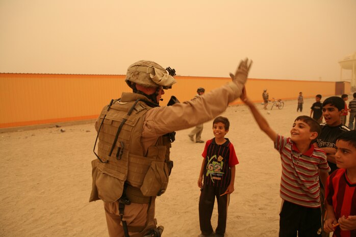 Cpl. Jonathan C. Austin, communications chief and convoy commander with Company B, Iraqi Transition Team 8, Regimental Combat Team 1, slaps an Iraqi child "hi-five" during a patrol through Fallujah June 9. Austin, a Lincolnton, N.C. native, took a few minutes with some transition members to play soccer with neighborhood children during the operation. (Official Marine Corps photo by Cpl. Chris T. Mann)