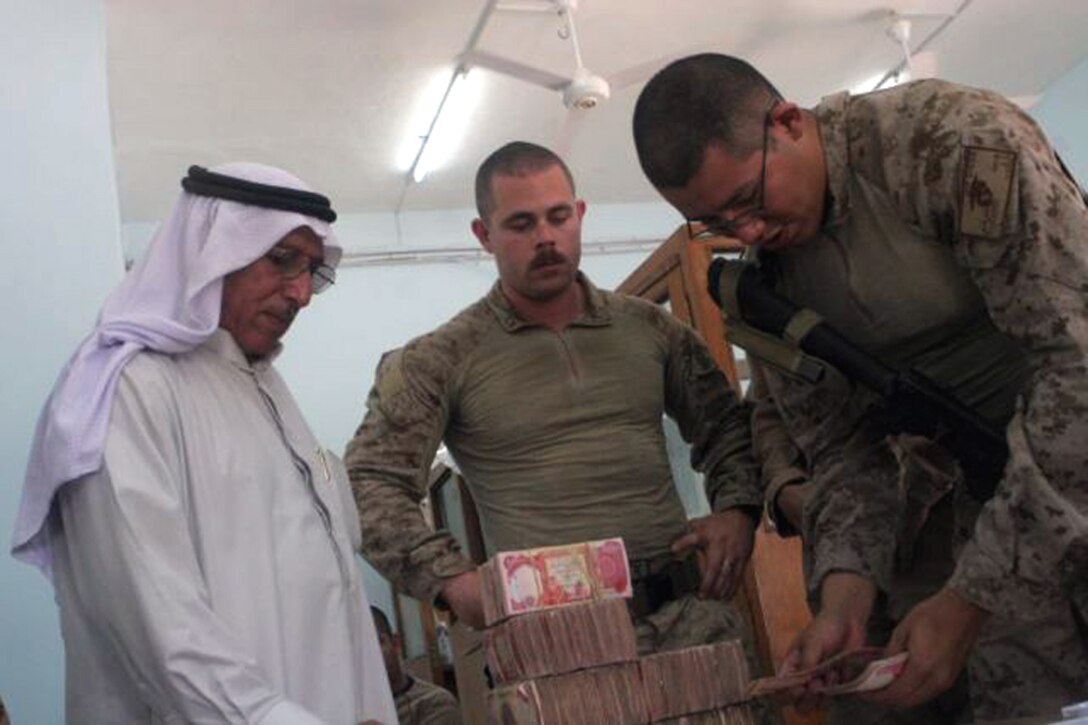 Hachem Aftan Alsherji, who works for the Al Batra'a company watches as Cpl. John C. Trevino, the disbursing noncommissioned officer in charge, Combat Logistics Battalion 6, 1st Marine Logistics Group, for Combat Outpost Rawah, counts out one of the stacks of Iraqi money as 1st Lt. Daniel M. Thomas, the team leader for Detachment 1, Civil Affairs Team 5, 2nd Battalion, 11th Marine Regiment, Regimental Combat Team 5, watches June 10. Hachem received payment for the contract work he and his company have completed on the bank and courthouse in the city of Rawah. The courthouse and bank are being refurbished before being turned back over to the local government. The buildings were previously used as posts by Coalition forces.