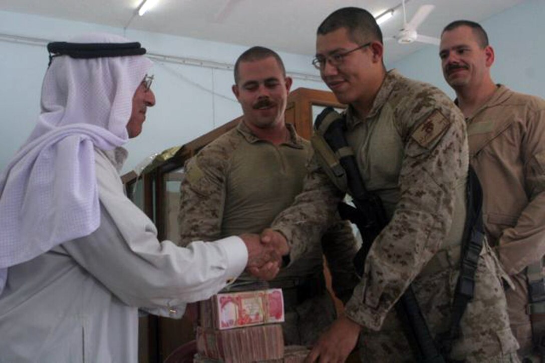 Hachem Aftan Alsherji, who works for the Al Batra'a company, shakes hands with Cpl. John C. Trevino, who is the disbursing noncommissioned officer in charge, Combat Logistics Battalion 6, 1st Marine Logistics Group, for Combat Outpost Rawah, as 1st Lt. Daniel M. Thomas, team leader, and Gunnery Sgt. Gary M. Gonzalez, staff noncommissioned officer in charge and assistant team leader, both with Detachment 1, Civil Affairs Team 5, 2nd Battalion, 11th Marine Regiment, Regimental Combat Team 5, watch the transaction June 10. Hachem received payment for the contract work he and his company have completed on the bank and courthouse in the city of Rawah. The bank project received its first payment and the courthouse project received its fourth. The payments are usually given in installments depending on the size of the project.