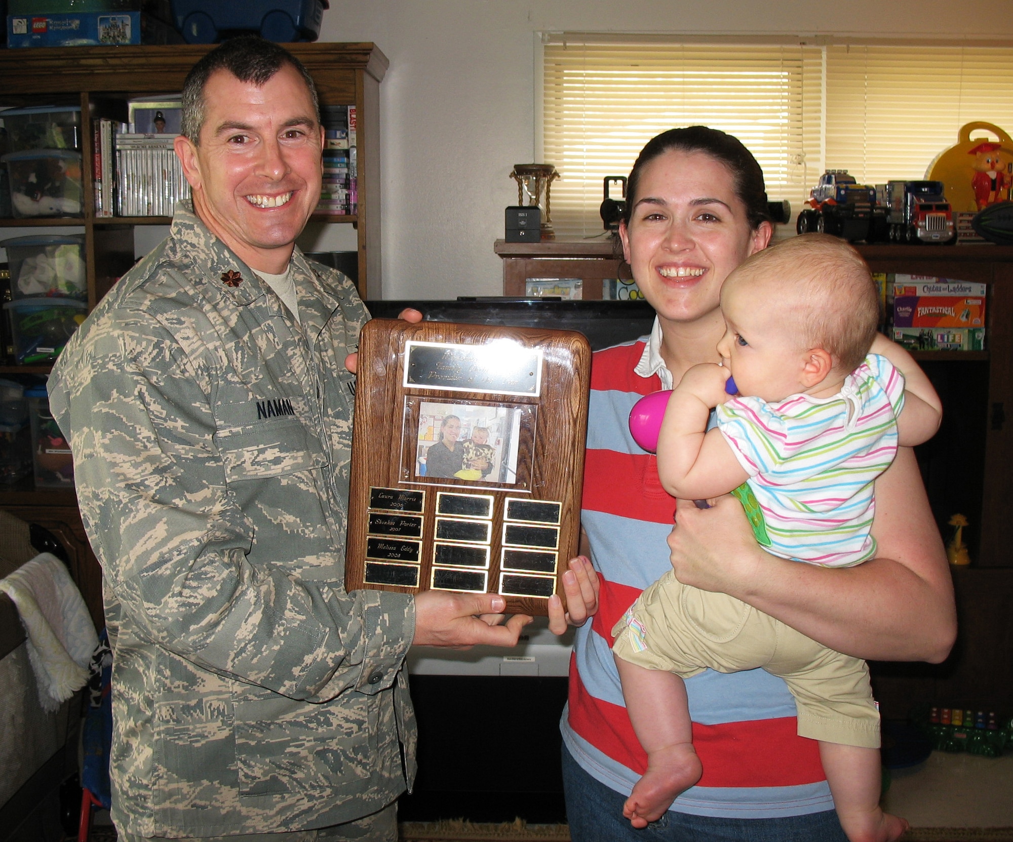WHITEMAN AIR FORCE BASE, Mo. -- Melissa Eddy, right holding Alice Warner, receives the Family Child Care Provide of the Year award April 21 from Maj. Kevin Naman, 509th Services Squadron commander. Licensed FCC is the care provided in base housing for one or more children of another person for more than 10 hours per week on a regular basis. The FCC staff ensures the quality of child care in base housing meets Air Force standards.Training is provided in child growth and development, protecting the health and safety of children, and child abuse prevention and reporting.