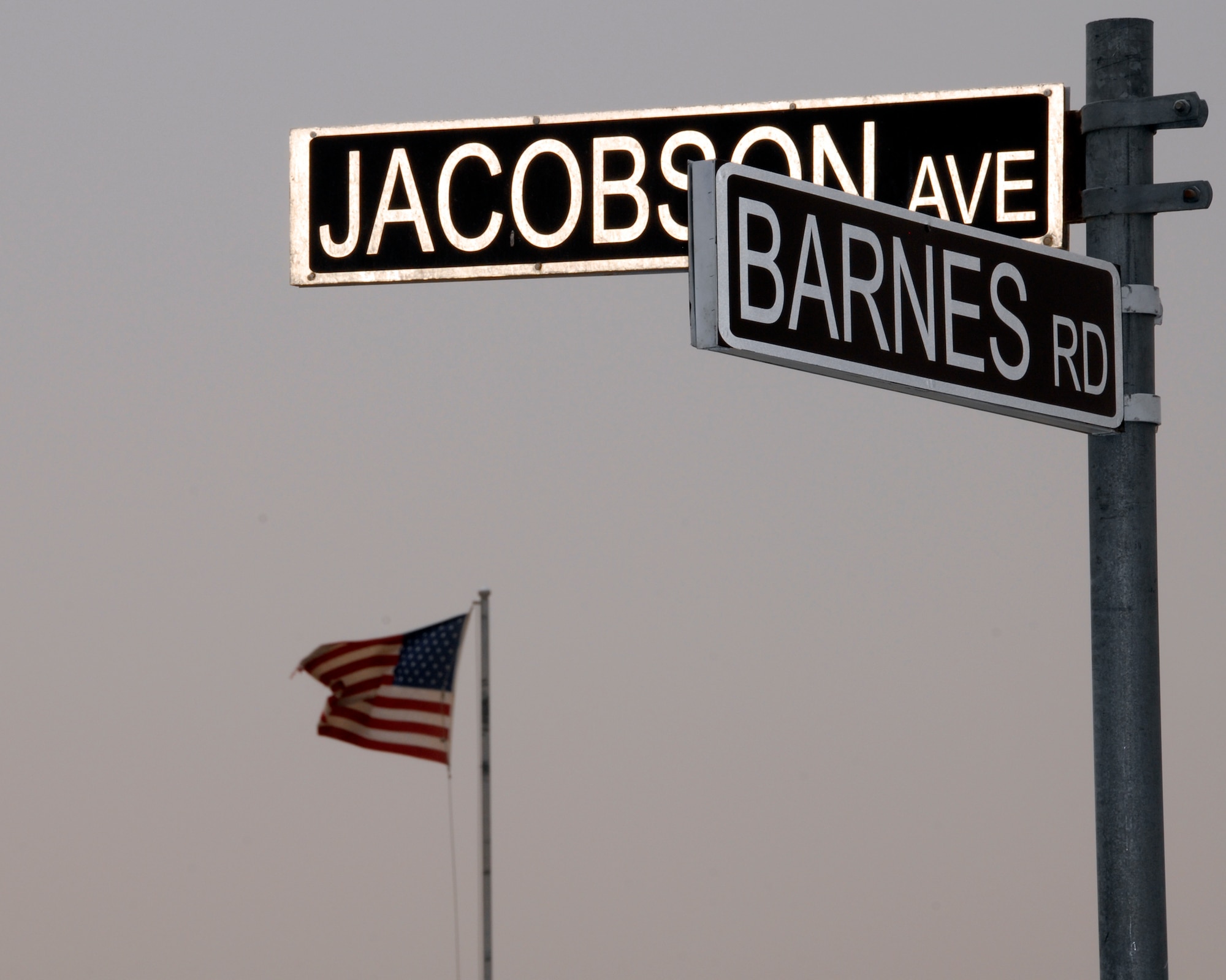 The U.S. flag waves proudly in the background behind the new Barnes Road and Jacobson Avenue intersection sign June 10 in Southwest Asia. The intersection is named in honor of Airman 1st Class Eric Barnes, who died June 10, 2007, as a result of an improvised explosive device attack on an Air Force convoy about 100 miles south of Baghdad, Iraq, and Airman 1st Class Elizabeth Jacobson, who died Sept. 28, 2005 while on a convoy near Camp Bucca, Iraq, when her vehicle was hit by an IED. She was the first female Airman killed in the line of duty in Operation Iraqi Freedom. (U.S. Air Force photo/Tech. Sgt. Michael O'Connor) 