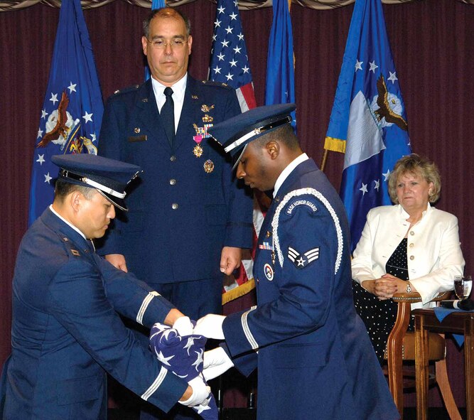 Col. Michael Hirka watches Tinker Honor Guard members Capt. Vanaryda Prom, left, and Senior Airman Saleem Salahuddin begin a flag folding ceremony during the 327th Aircraft Sustainment Group commander’s June 2 retirement ceremony. Officiating over the ceremony in the Tinker Club was Sue Payton, assistant secretary of the Air Force for Acquisition at the Pentagon.  Ms Payton once worked for Col. Hirka in the early years of their government service.  (Air Force photo by Margo Wright)
