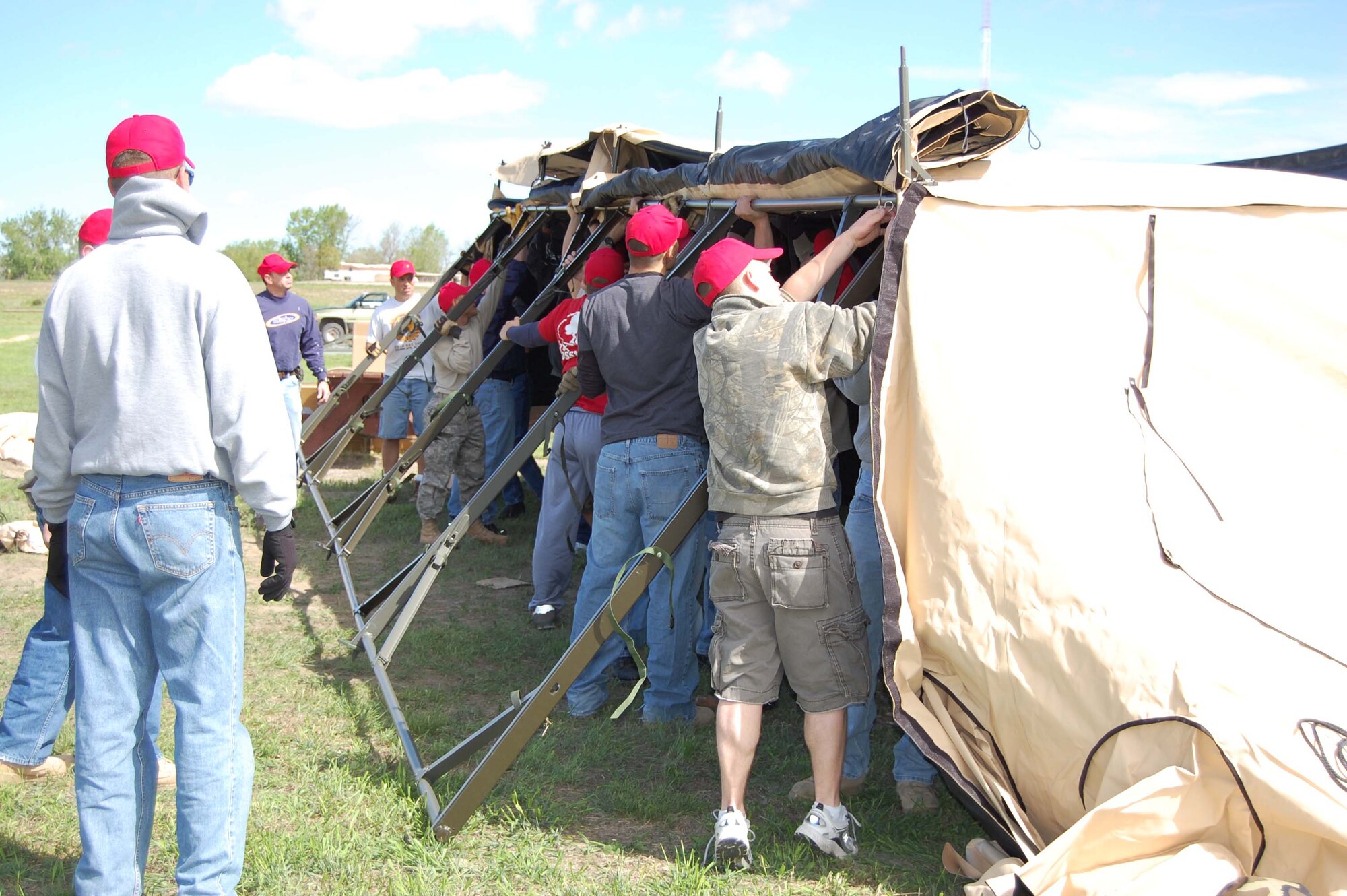 After nearly an hour of teamwork, the first side of the four-panel tent is stood up and secured prior to standing up the second side. The 819th RED HORSE Squadron lent two of their tents to the Montana Fish, Wildlife and Parks personnel in support of their annual kid's fishing day at Wadsworth Pond June 7. (U.S. Air Force photo/Valerie Mullett)