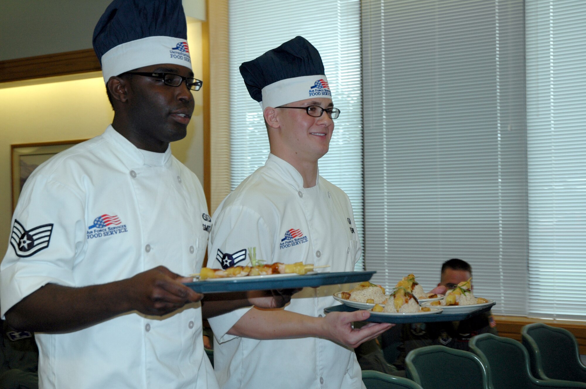 Staff Sgt. Jeremy Smith and Airman 1st Class Joe Klien, 12 Missile Squadron, walk to the judges table with their award-winning Asian barbecue shrimp with coconut rice during the Warrior Chef competition at the Elkhorn Diner June 10. (U.S. Air Force photo/Airman 1st Class Emerald Ralston)