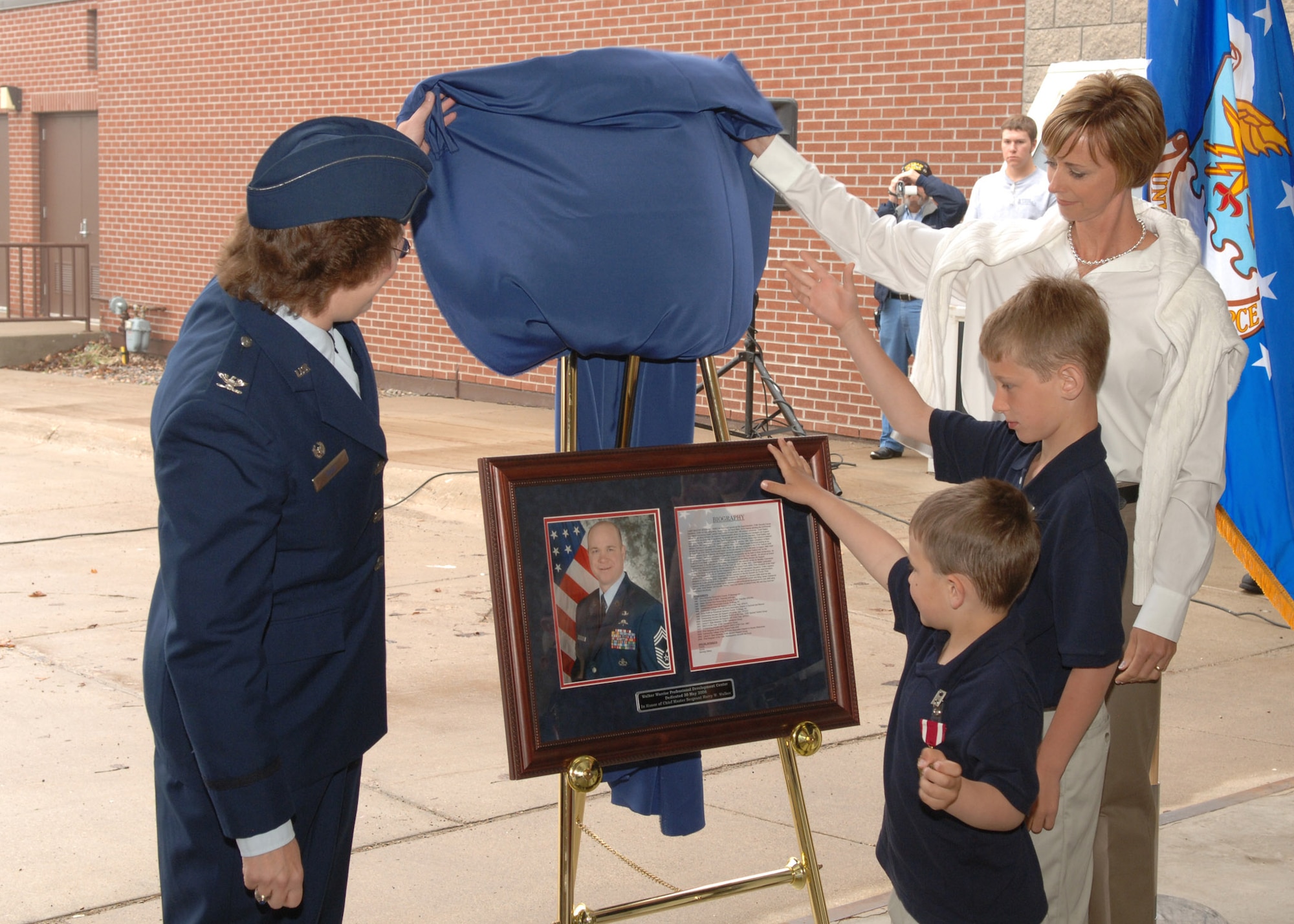 GRAND FORKS AIR FORCE BASE, N.D. – Col. Diane Hull (left) and Mrs. Tracey Walker and her two sons unveil a dedication to Chief Harry Walker. The First Term Airman Center was renamed the Walker Professional Development Center during a ceremony here May 30 to honor an Airman who had a profound impact on the wing. (U.S. Air Force photo/Senior Airman Chad Kellum) 