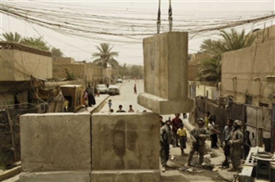 U.S. Army soldiers guide a concrete barrier down into position as a crane lowers it to a street opening near the Joint Security Station in Shula, Iraq, on June 8, 2008.  