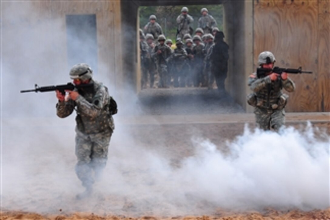 U.S. Army Staff Sgts. Patrick Sumey and Terry Cooper, both instructors for the pre-deployment training assistance element initiative, sprint through the fog from a smoke canister as students and instructors view from the starting point at Camp Grayling, Mich.  The soldiers are training for deployment by participating in the National Guardís new pre-deployment training assistance element program.  