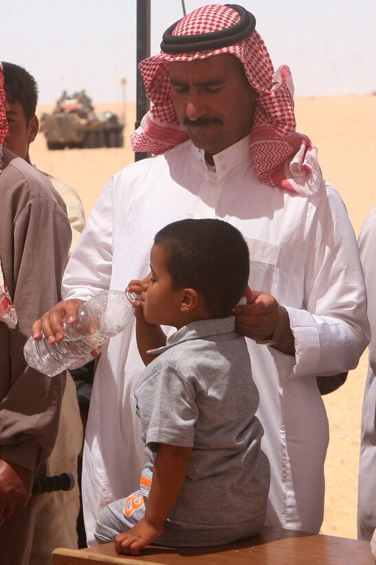 Razaq Naghmash Kanoush, a resident of Nathara, Iraq, gives his son a drink from a bottle of water provided to him by Coalition forces during a medical support operation in the village of Nathara, Iraq, June 12.  Setting up a large tent in the middle of the town, the service members provided Iraqi men and women of all ages with water, medical diagnosis and medicine.