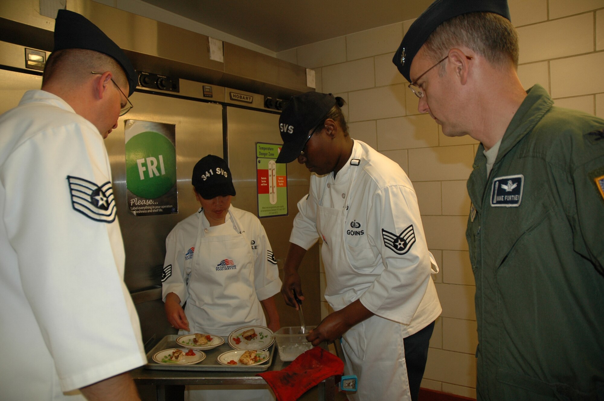 Tech. Sgt. Donnie Parish, 341st Operations Support Squadron, and Col. Michael Fortney, 341st Space Wing commander, look on as Staff Sgt. Rowena Hawley and Staff Sgt. Ebony Goins, 341st Services Squadron, prepare their entrees for presentation to the judges at the Warrior Chef competition June 10 at the Elkhorn Diner. (U.S. Air Force photo/Airman 1st Class Emerald Ralston)
