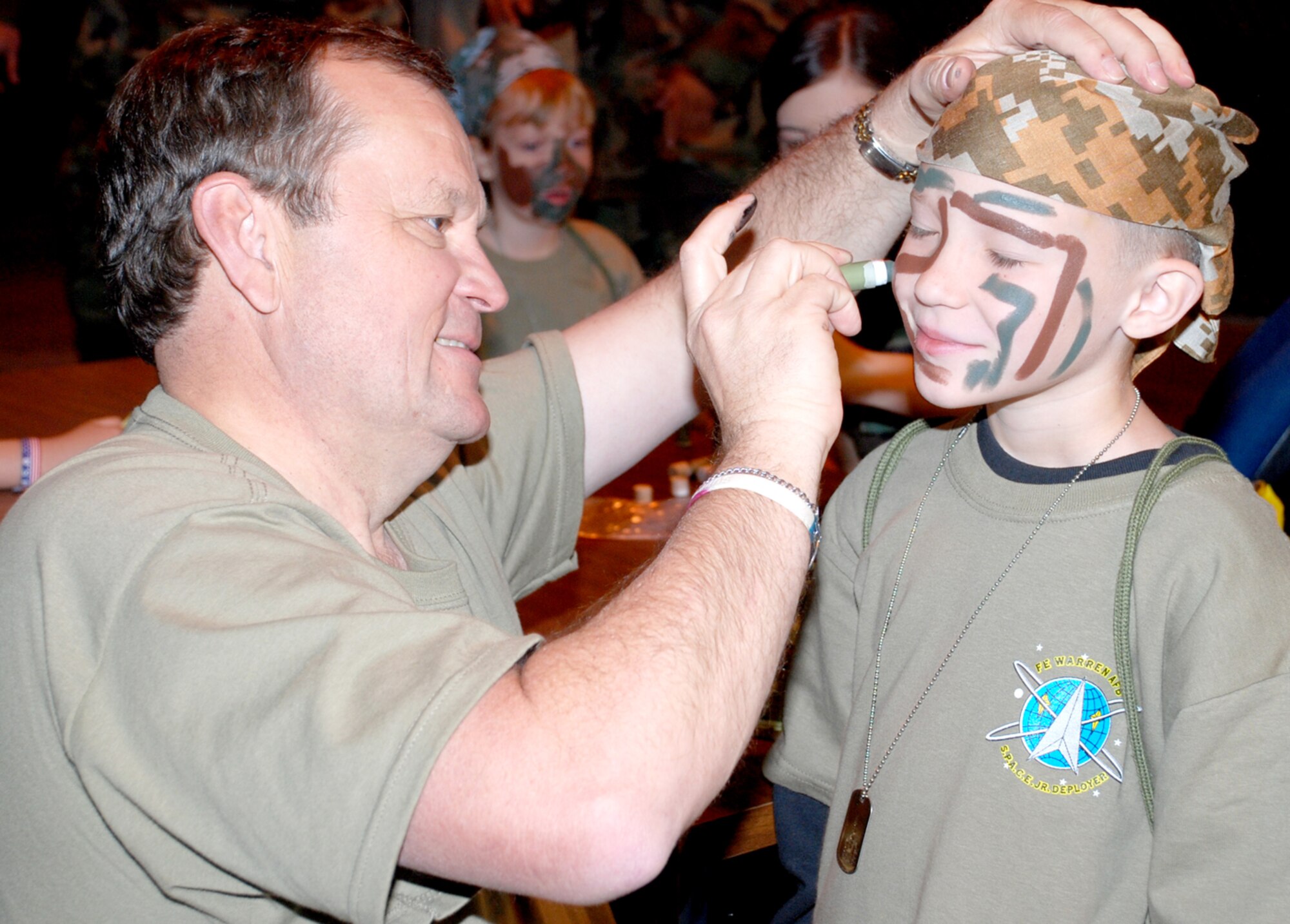 Randy Shircel, 90th Force Support Squadron deputy commander, paints the face of a Jr. Deployer during the processing line. While the deployers processed through, base agencies including the medical clinic, the chaplain office, finance and the Airman and family readiness center provided information and supplies.