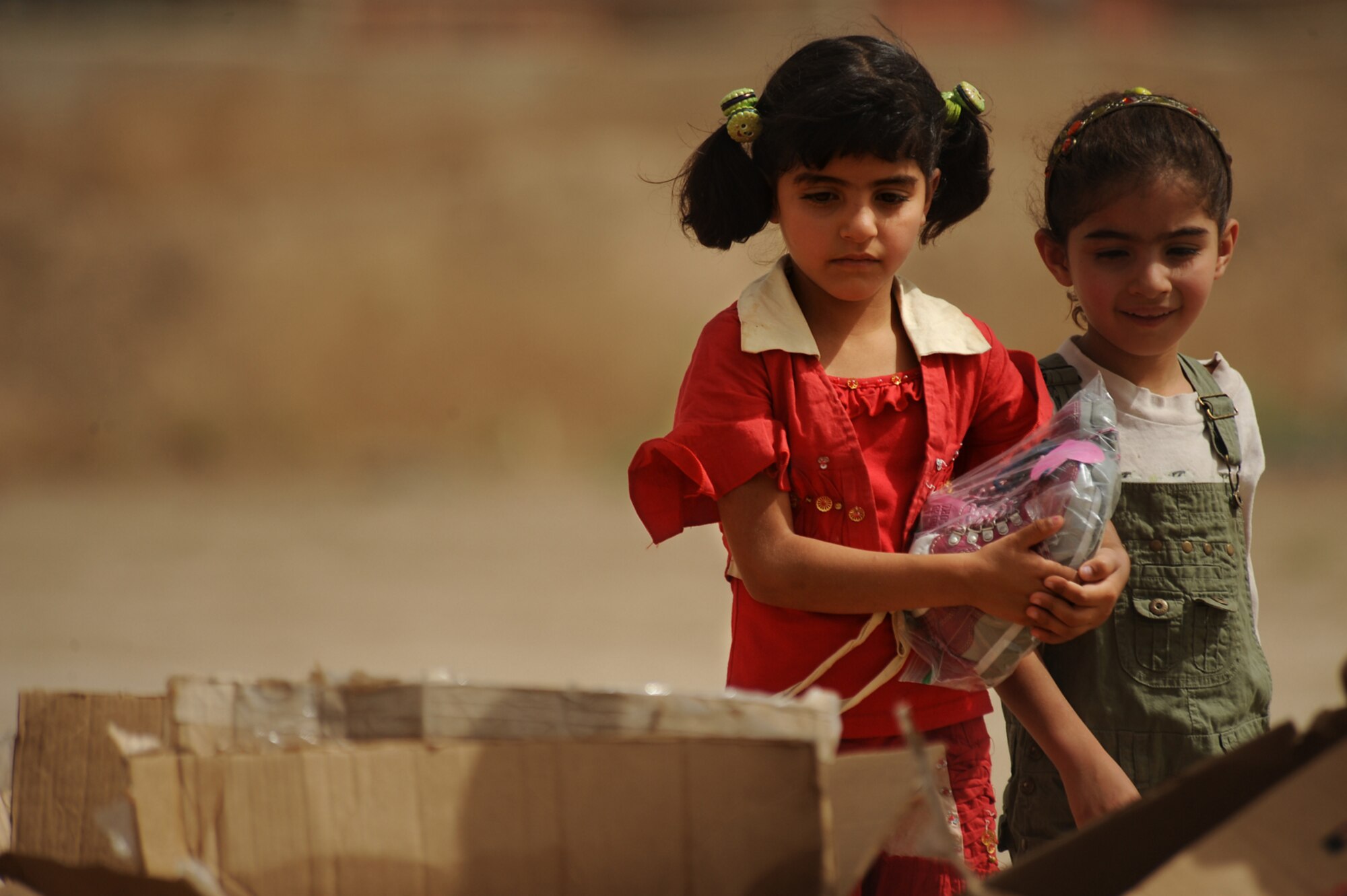 SATHER AIR BASE, Iraq -- Two young Iraqi girls look through boxes of toys and gifts donated by Airmen here June 6. The gifts were donated and delivered as part of the Good Neighbor Program at Sather AB. (U.S. Air Force photo/Tech. Sgt. Jeffrey Allen)