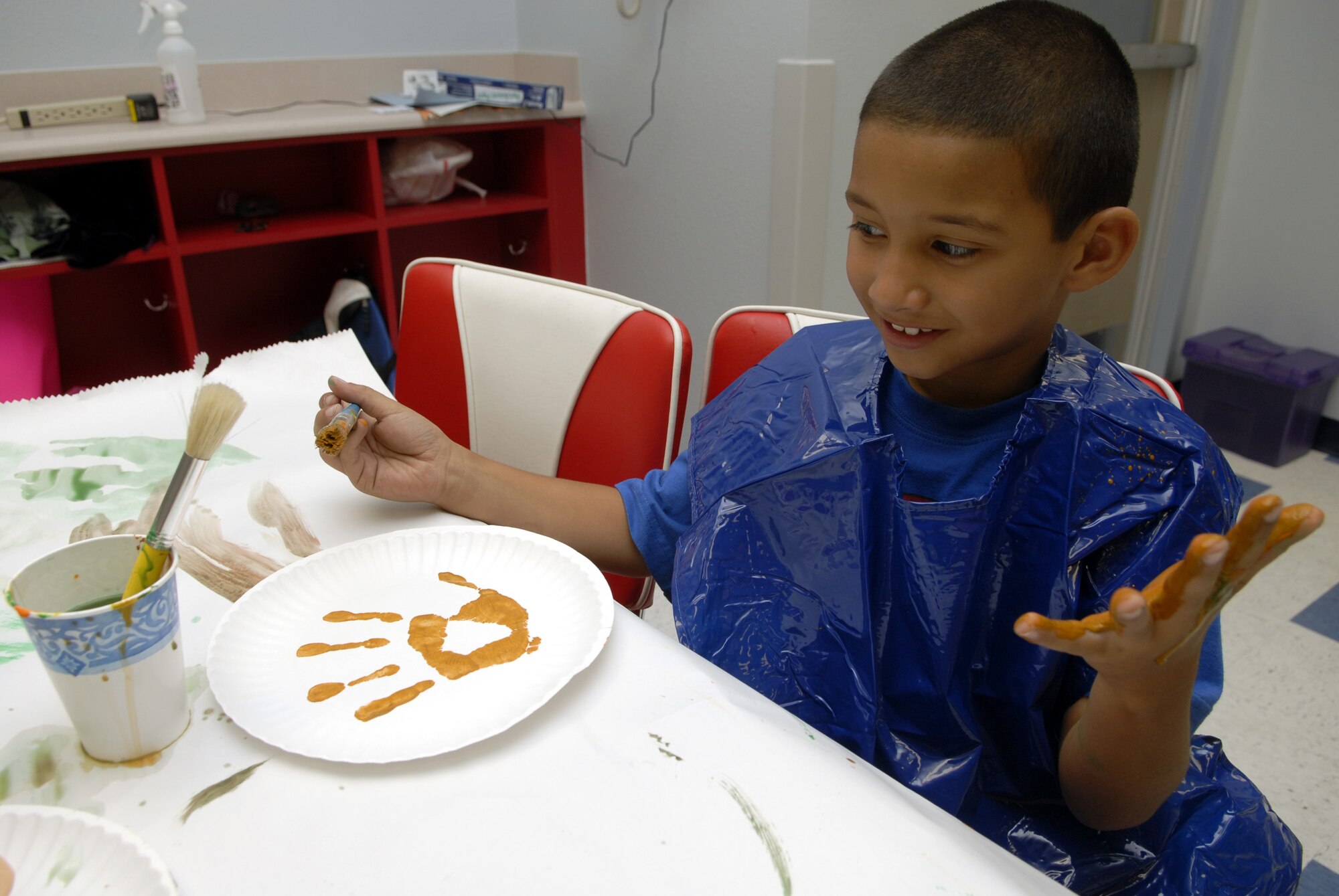 Six-year old Derek Alemany, paint brush in one hand, uses his other hand to express himself during arts and crafts time at the school-age facility. (U.S. Air Force photo by Senior Airman Kamaile Chan)