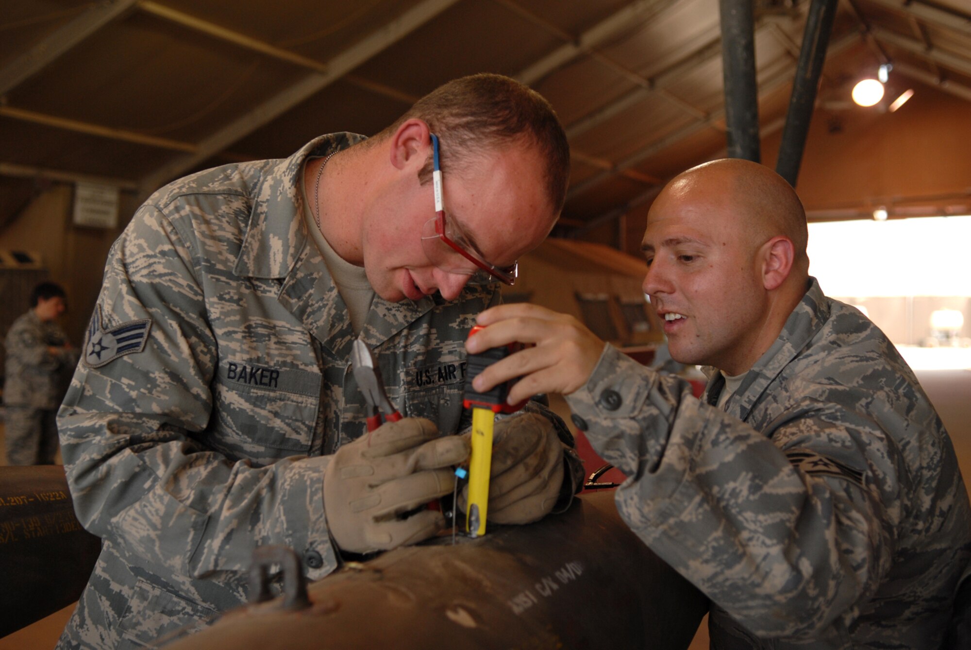 JOINT BASE BALAD, Iraq -- Senior Airman Nathan Baker and Staff Sgt. Jose Landeros, 332nd Expeditionary Maintenance Squadron munitions systems specialists, measure the length of a GBU-12 arming lanyard to a bomb body here, June 16. This measurement varies based on the aircraft to which the munition is attached. The GBU-12 is a laser-guided munition. Airman Baker is deployed from Hill Air Force Base, Utah; Sergeant Landeros is deployed from Shaw Air Force Base, S.C. (U.S. Air Force photo/ Senior Airman Julianne Showalter)