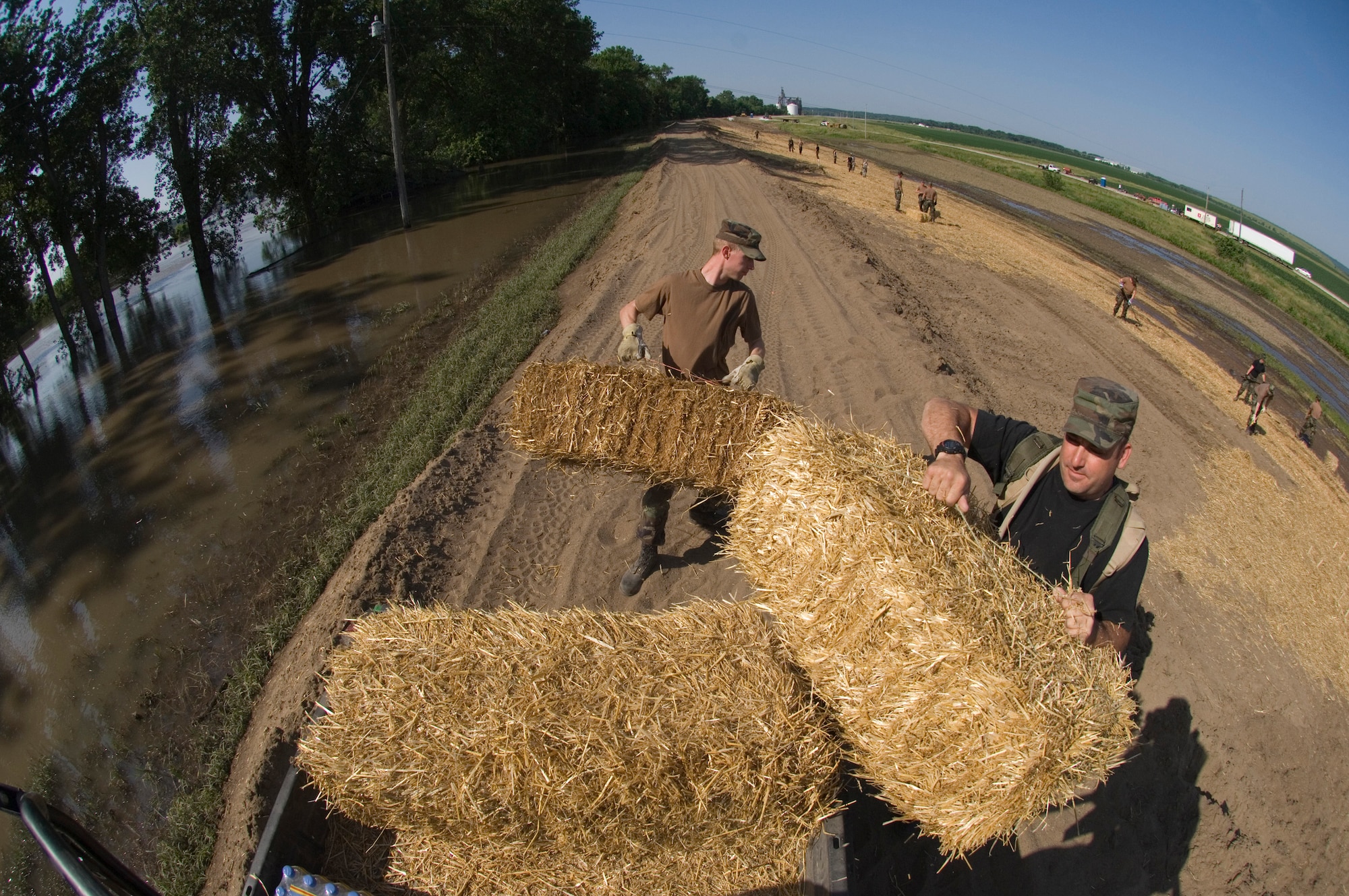 Staff Sgts. Troy Martin (right) and Cody Sorenson unload bails of hay to be used for erosion control near the Mississippi River June 18 in Burlington, Iowa. Approximately 14,000 acres of farmland is in danger of erosion if the flooding is not controlled. Sergeants Martin and Sorenson are both assigned to the Iowa Air National Guard's 185th Services Squadron in Sioux City, Iowa. (U.S. Air Force photo/Master Sgt. Jack Braden) 