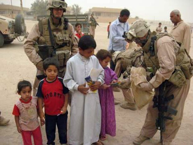 Lance Cpl. Nick Folse (left), an intelligence analyst with 2nd Battalion, 24th Marine Regiment poses for a photo with local Iraqi children while Cpl. Marco Vallejo passes out school supplies to the kids. School supplies were donated by teachers and students of the Oswego, Ill., Public School District #308 to give to the children.::r::::n::